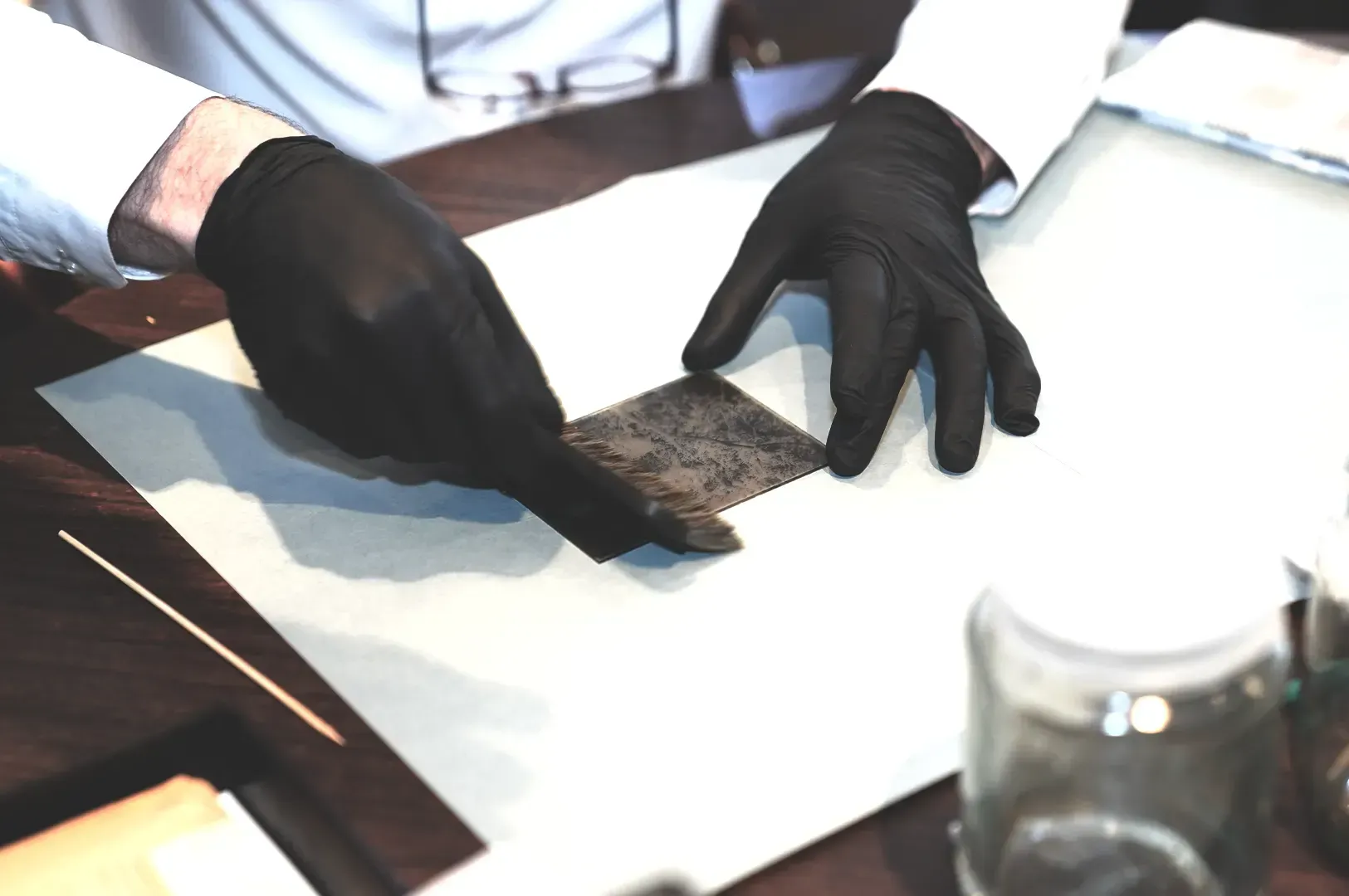 Close-up shot of a craftsperson wearing black protective gloves delicately cleaning a weathered meta