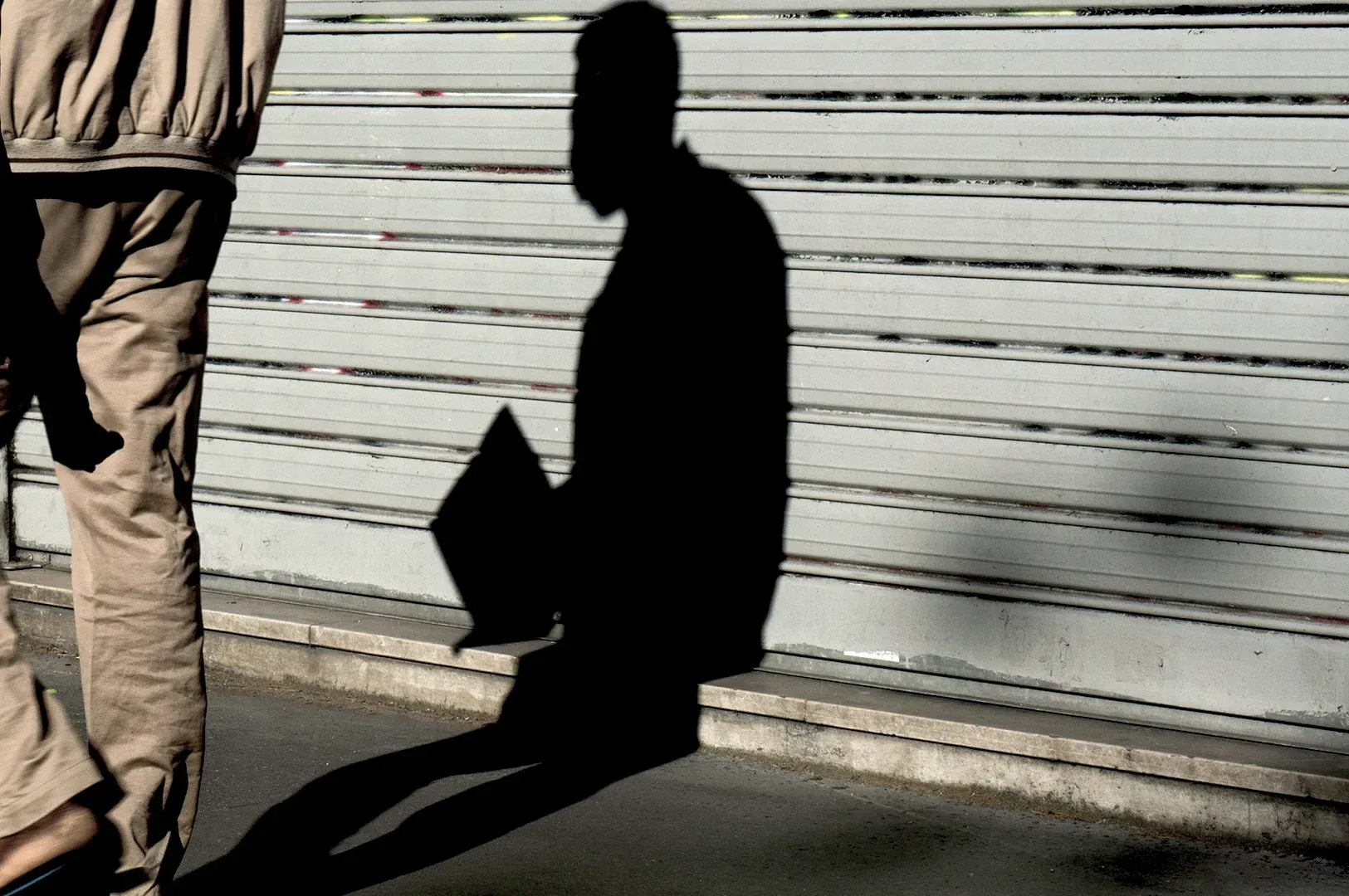 A stark, dramatic silhouette of a person walking past a shuttered shopfront, symbolizing the contemp