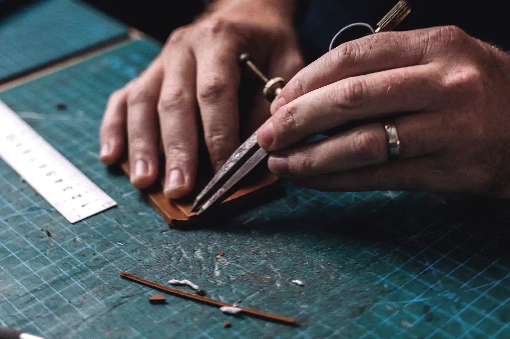 A leather artisan using precision divider tools and a ruler on a cutting mat to meticulously measure