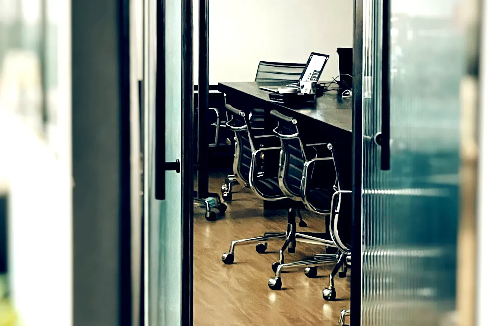 Looking through glass doors into an empty corporate conference room with black leather chairs and la
