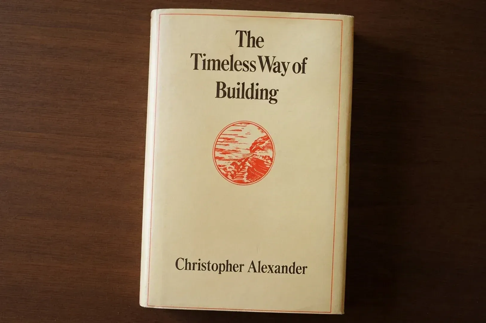 The hardcover book 'The Timeless Way of Building' by Christopher Alexander resting on a dark wooden