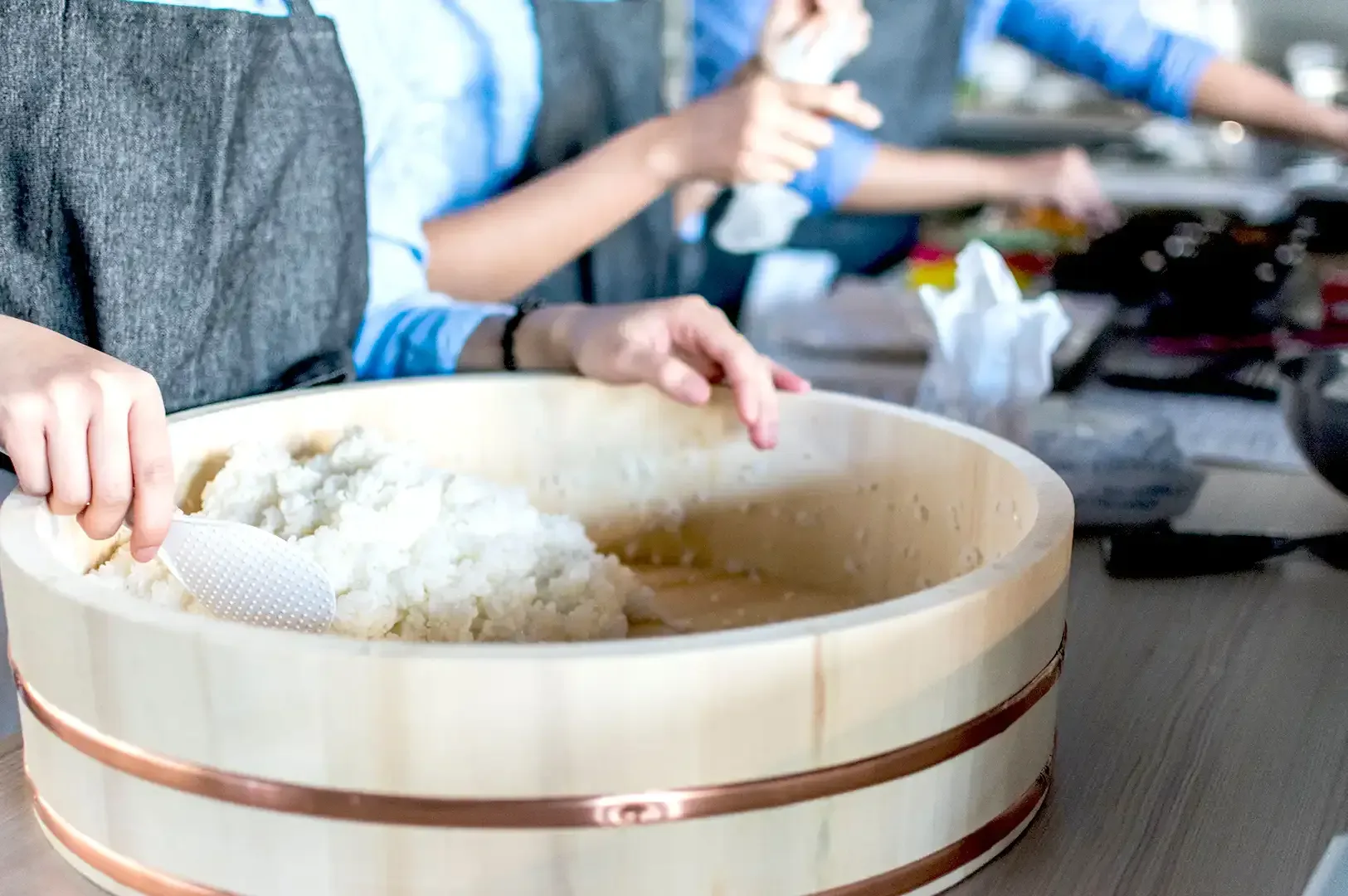 A chef carefully mixing seasoned rice in a traditional wooden hangiri tub, illustrating the patient