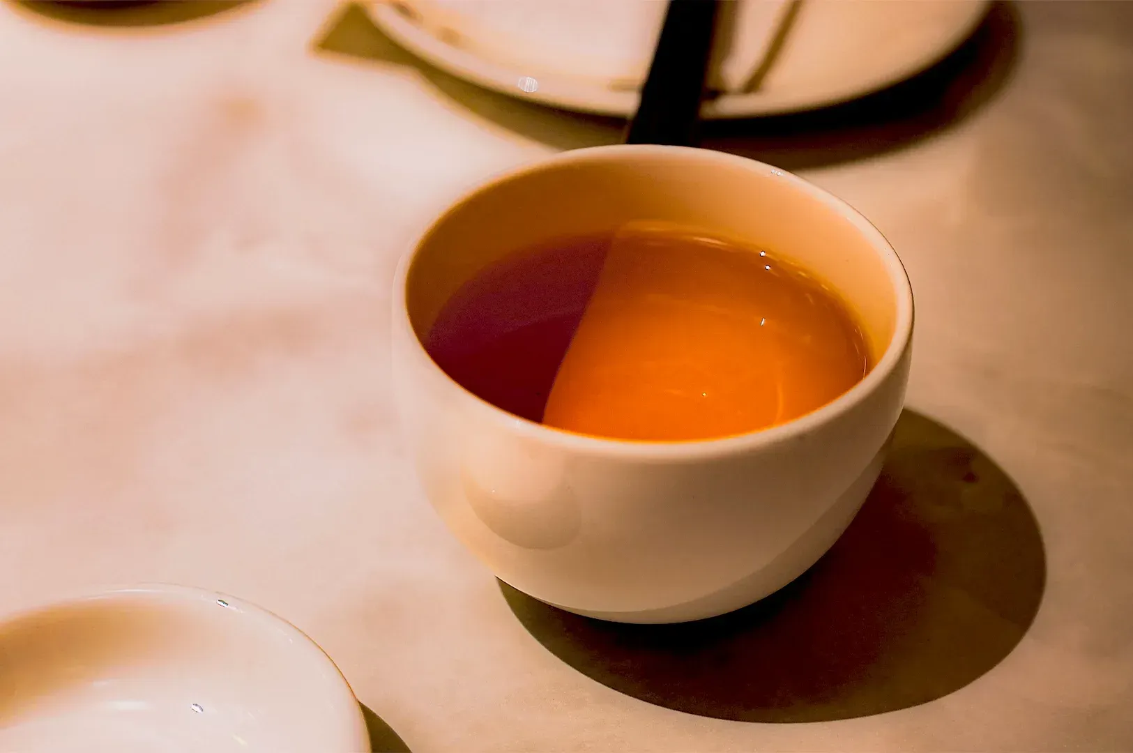 A minimalist, warm-toned close-up of a simple ceramic tea cup on a table, symbolizing the quiet beau