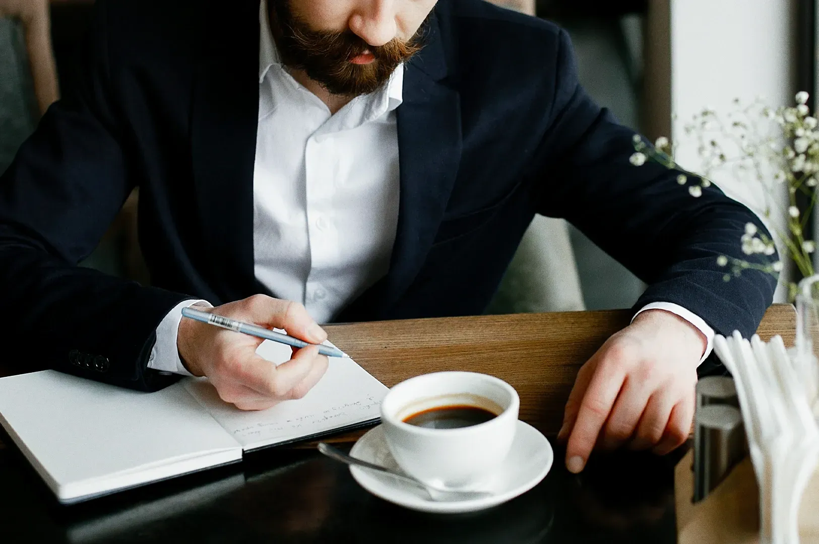 Close-up high-angle shot of a professional writing in a journal beside a coffee cup, illustrating fi
