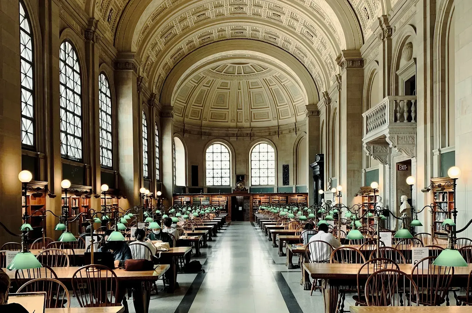 Grand historic reading hall with high arched ceilings, long rows of wooden tables, green study lamps