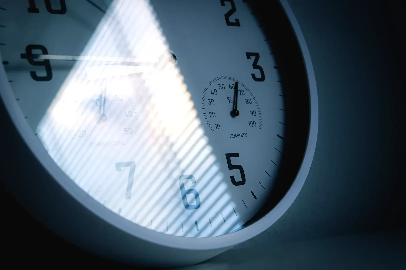 Close-up of an analog clock and humidity gauge with soft window shadows, symbolizing the patience, precision, and environment required for high-quality, thoughtful craftsmanship.