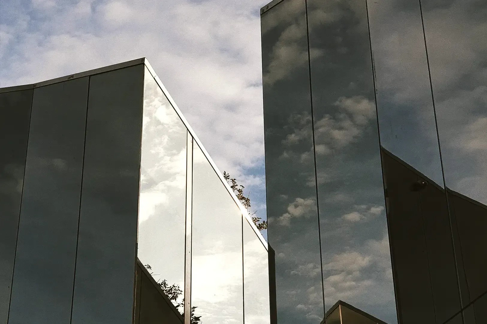Modern glass architectural panels reflecting a cloudy blue sky, symbolizing reflection and self-awareness in mentorship.