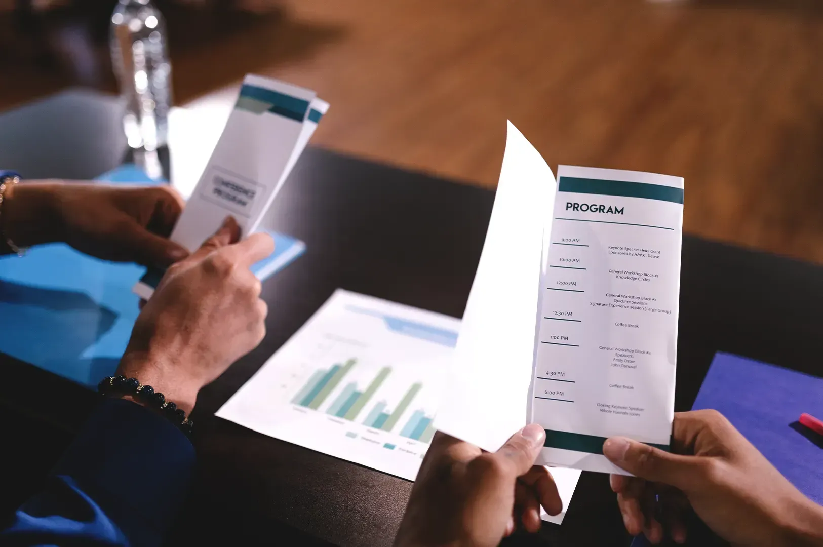 Hands holding a conference program guide over a desk with business charts, representing how naming desire and returning to craft turns comparison into a compass.