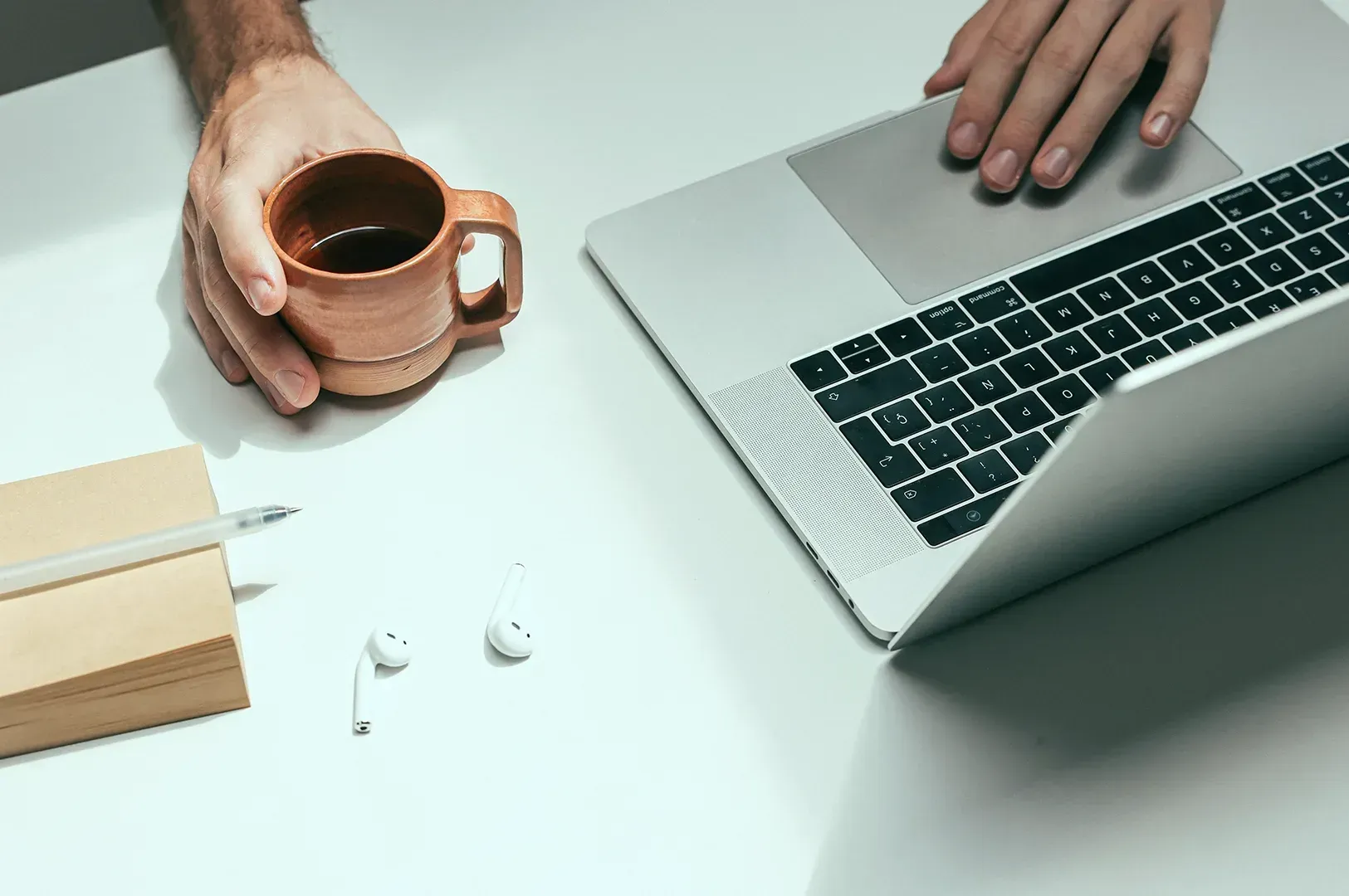 Overhead view of a minimalist workspace showcasing a person holding a cup of coffee, laptop, and notebook, symbolizing deliberate creative focus and rituals for better productivity.