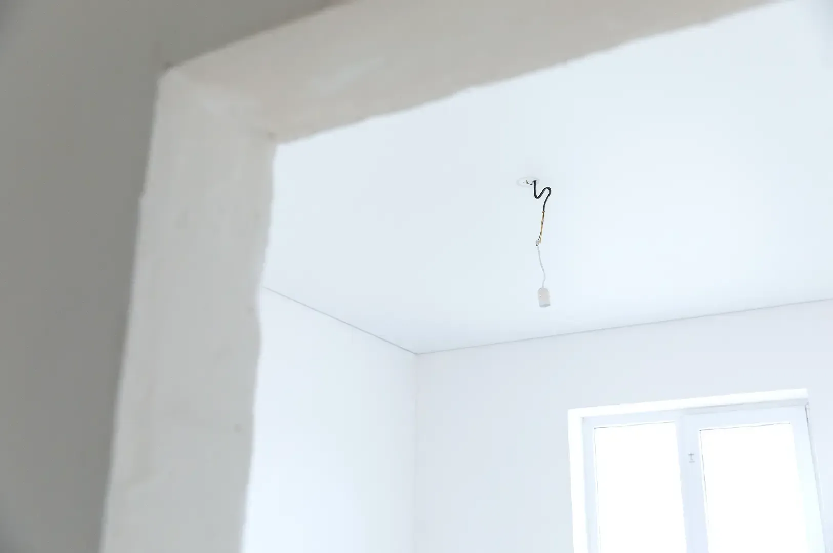 A minimalist white room in construction with a single bare light bulb hanging from the ceiling, symbolizing uncompromised simplicity and the foundational discipline of keeping standards intact.