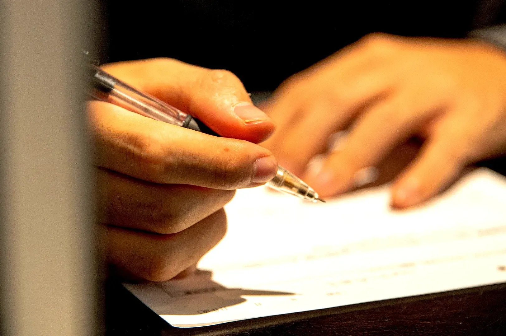 A person's hand focused on writing carefully on a document, symbolizing the deliberate act of planning, standard-setting, and communicating professional value through thoughtful, human-centered work.