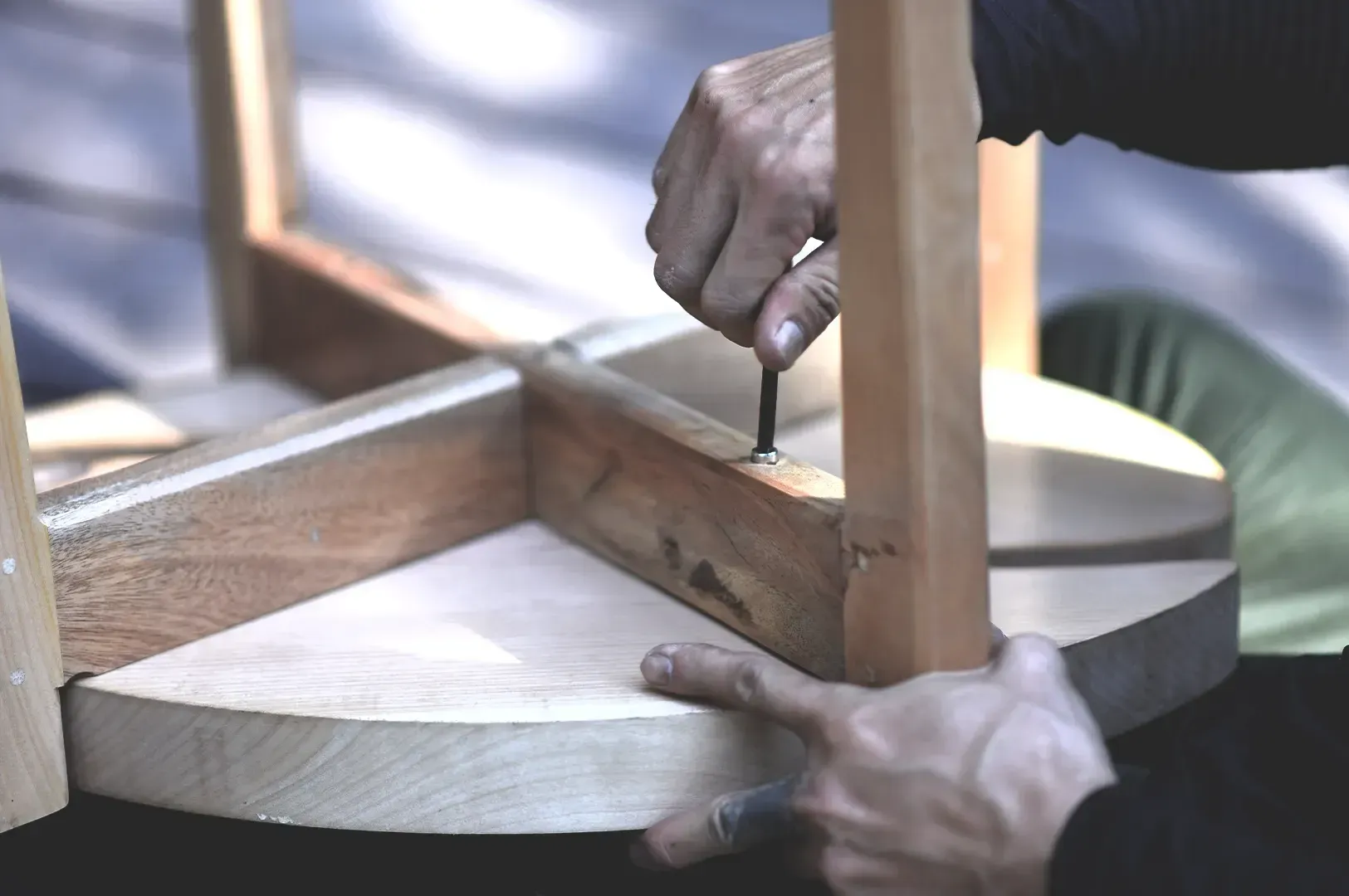 Close-up view of hands assembling and tightening a bolt on a wooden furniture frame with an allen key, reflecting the practical longevity and care inherent in making things last.