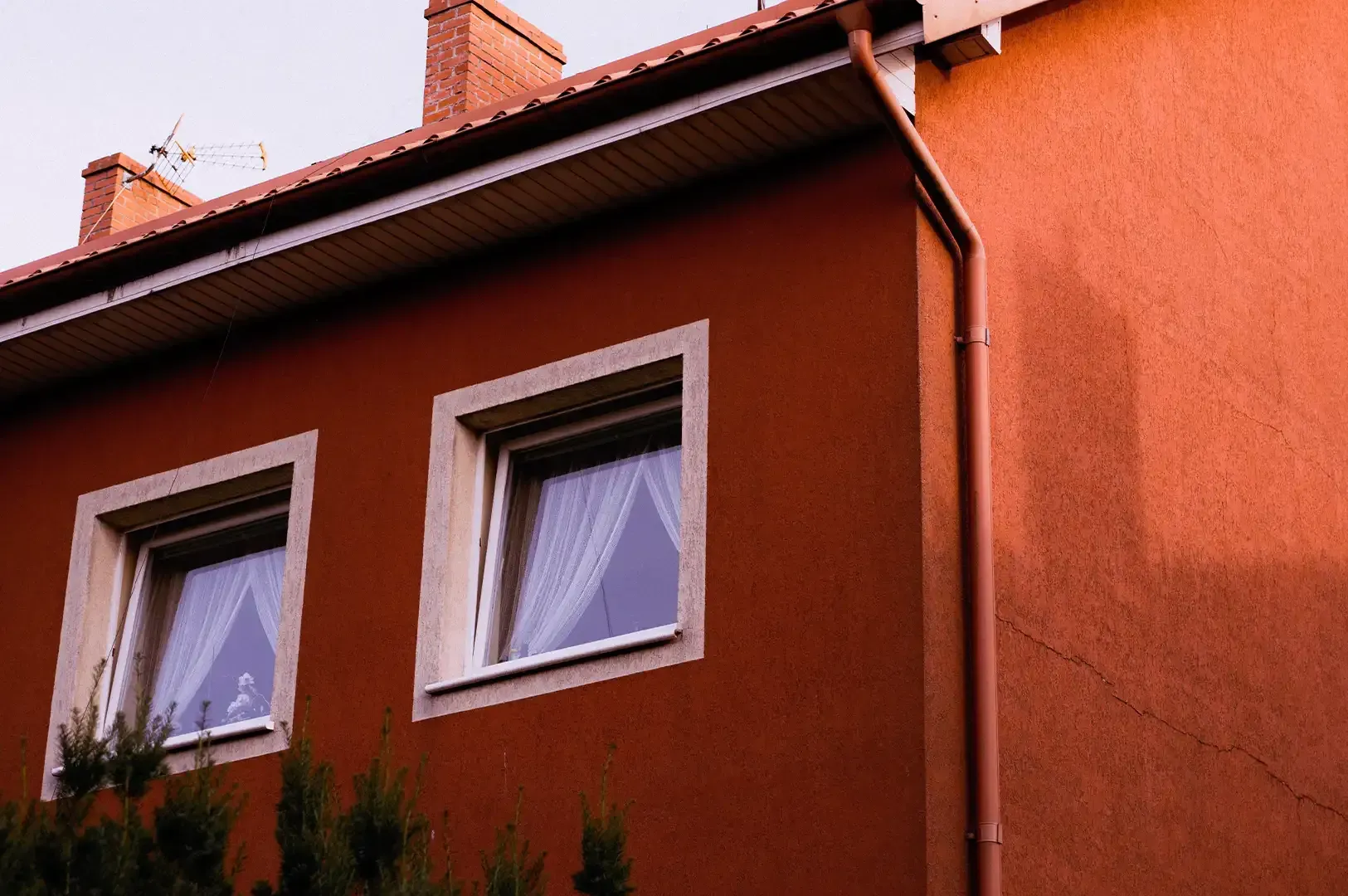 A view of house windows on a textured red exterior, evoking the themes of Gaston Bachelard's The Poetics of Space regarding how domestic architecture influences our inner lives and imaginative experiences.