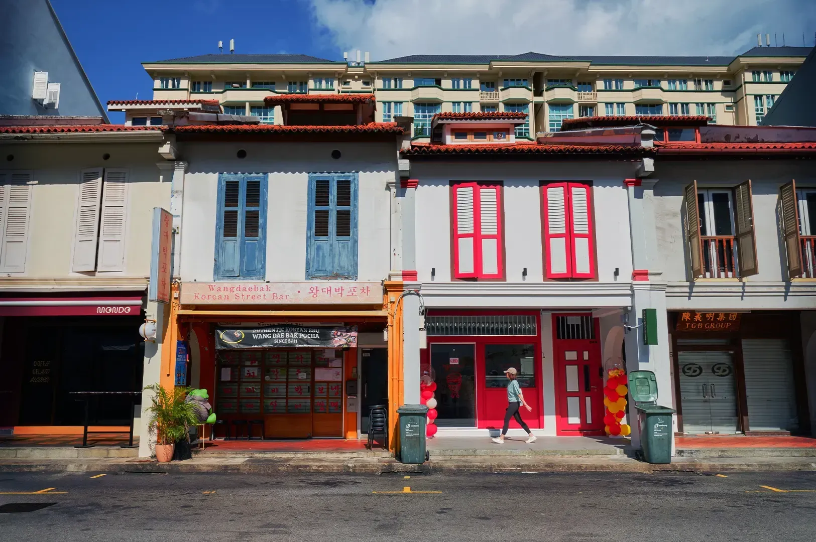 A person walking slowly down a vibrant street of traditional shophouses, capturing the essence of walking as inquiry and the unexpected discoveries found when we allow a city to interrupt our path.