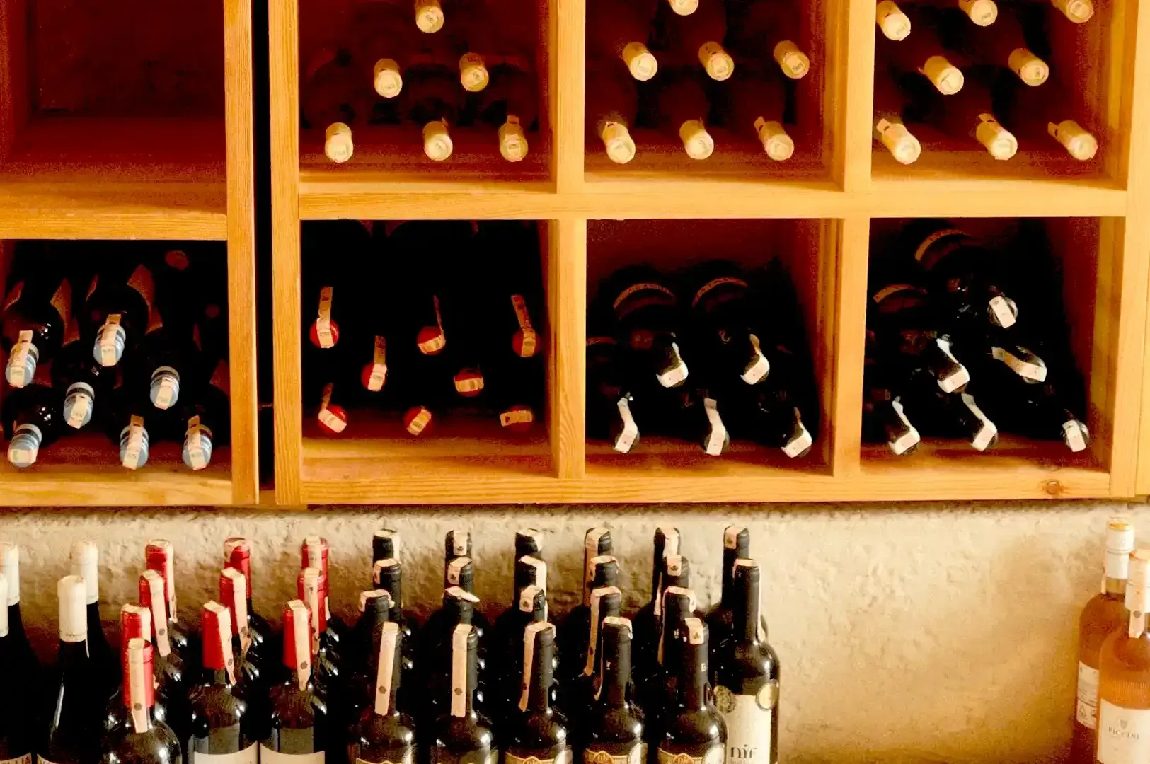 A wooden wine rack filled with neatly organized bottles of red and white wine, showcasing a collection built on restraint and aging.