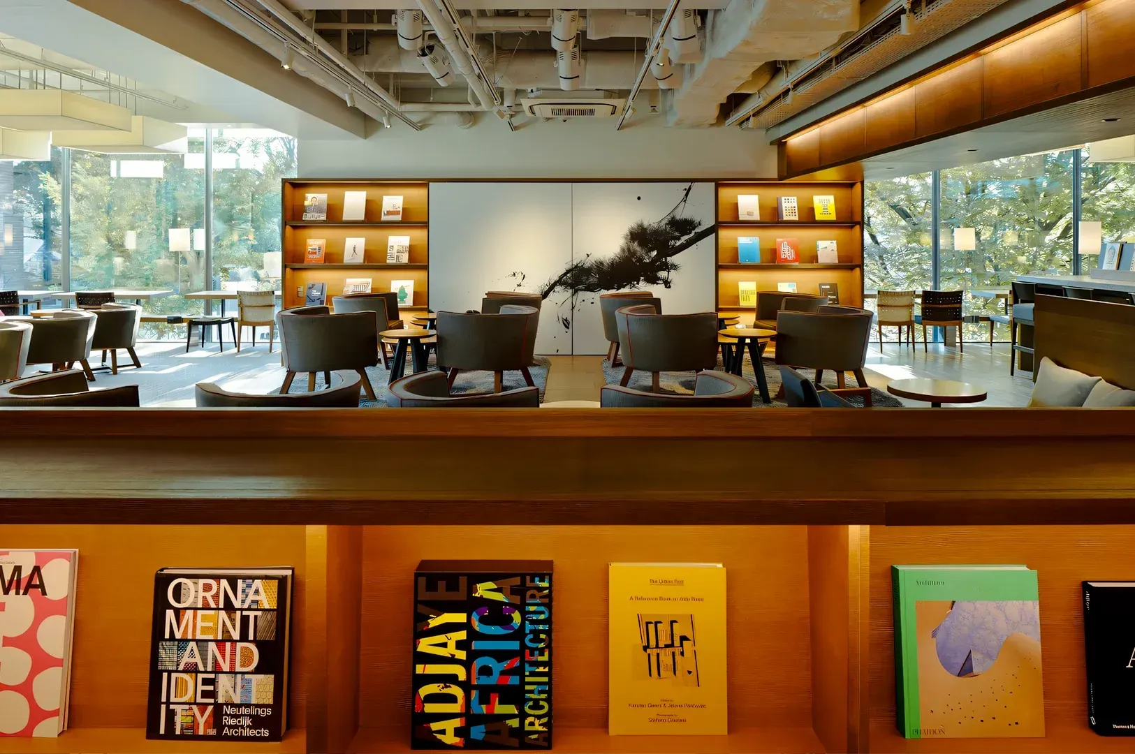 Modern reading lounge with floor‑to‑ceiling windows, curated bookshelves, wooden furniture, and contemporary art centerpiece.