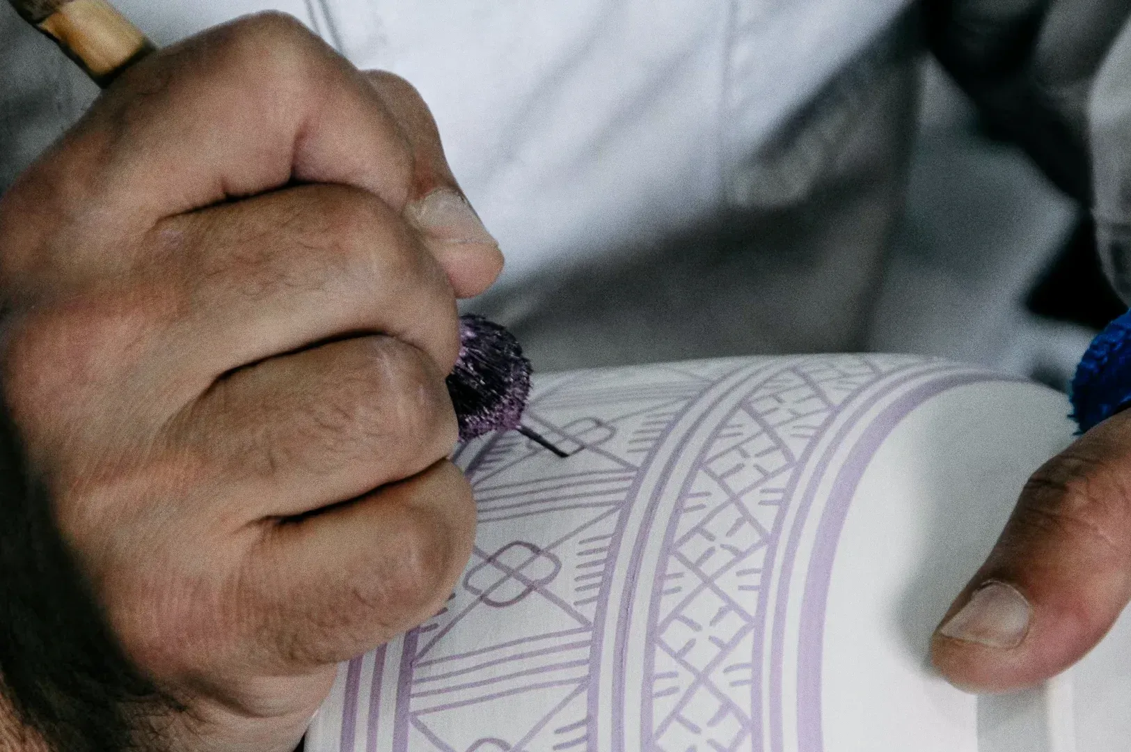 Extreme close-up macro shot of hands painting intricate ceramic patterns, representing artisan craftsmanship, cultural respect, and the mindful traveler’s choice to observe rather than consume.