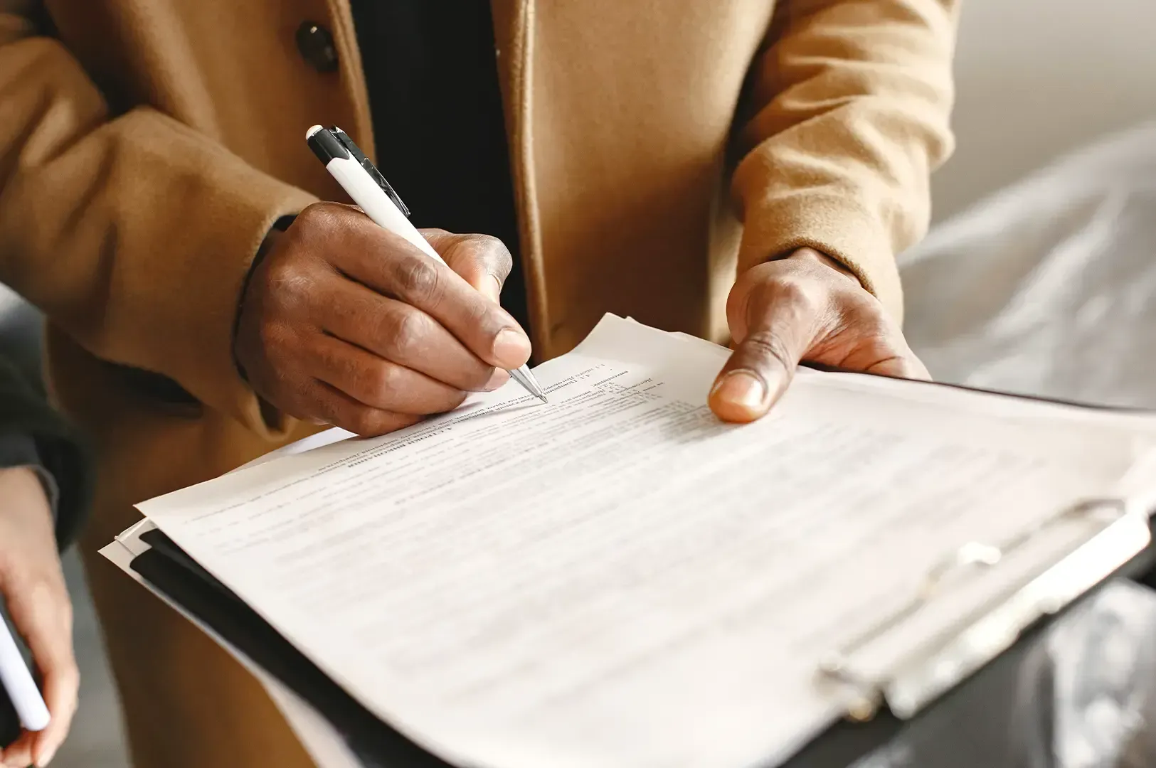 A person in a camel coat signing a formal agreement on a clipboard, capturing the crucial moment when accountability is finalized and holding the line prevents long-term compromise.