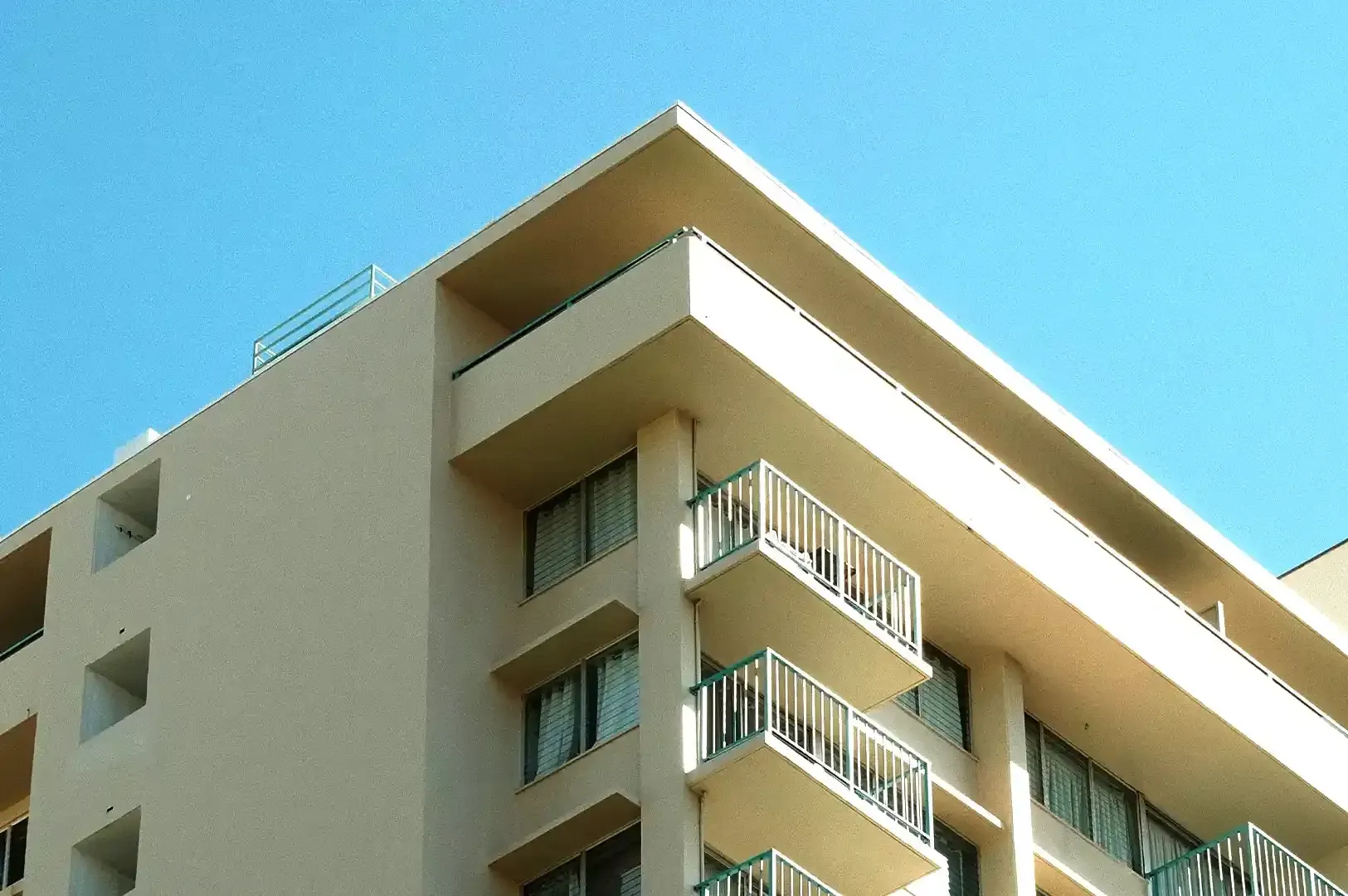 A modern architectural building corner with clean geometric lines and balconies under a clear sky, embodying the enduring architectural principles of Christopher Alexander.