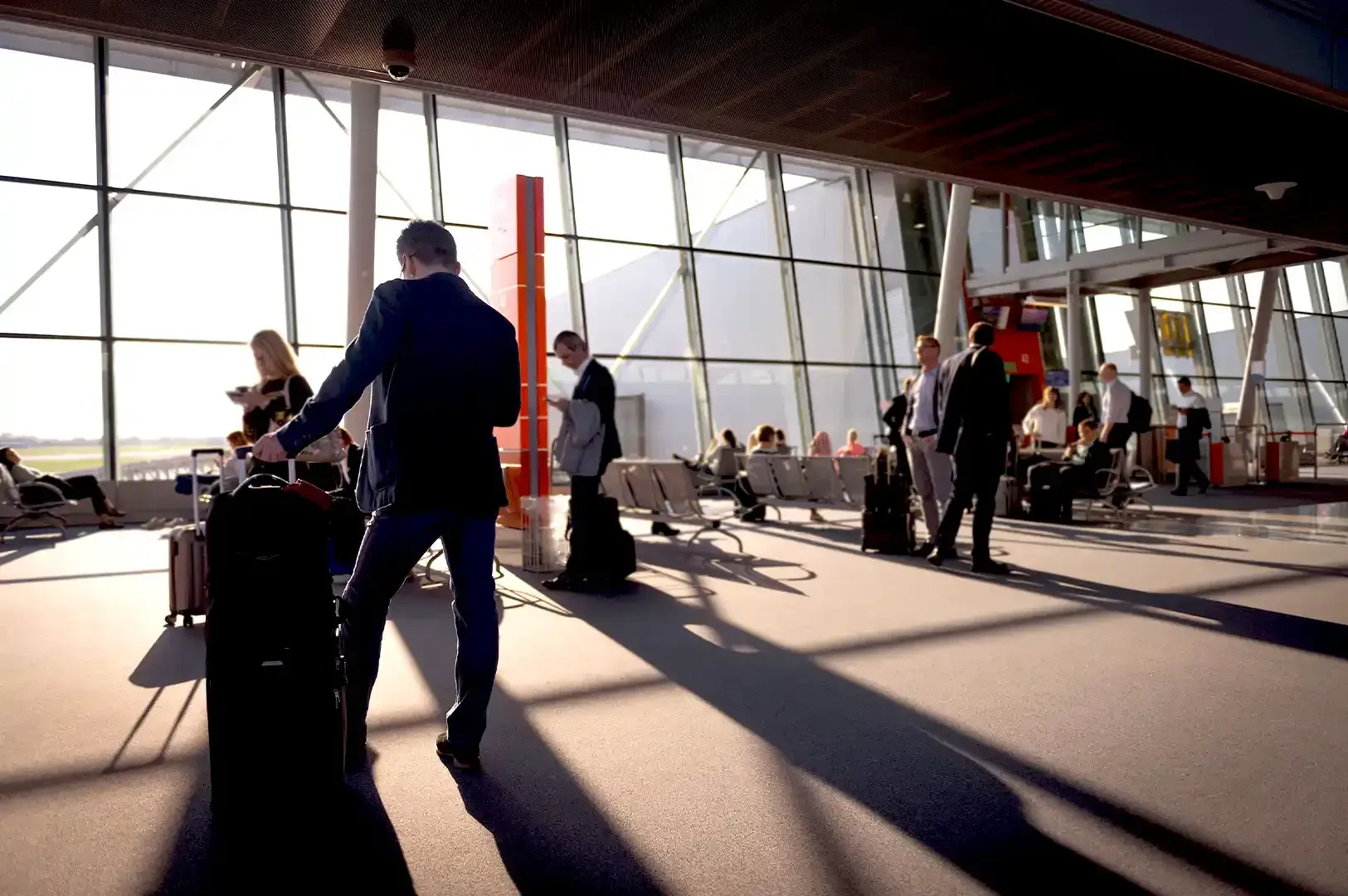 A traveler pulling a rolling suitcase through a sunlit airport terminal with large glass windows, illustrating the freedom of carrying less while on the move.