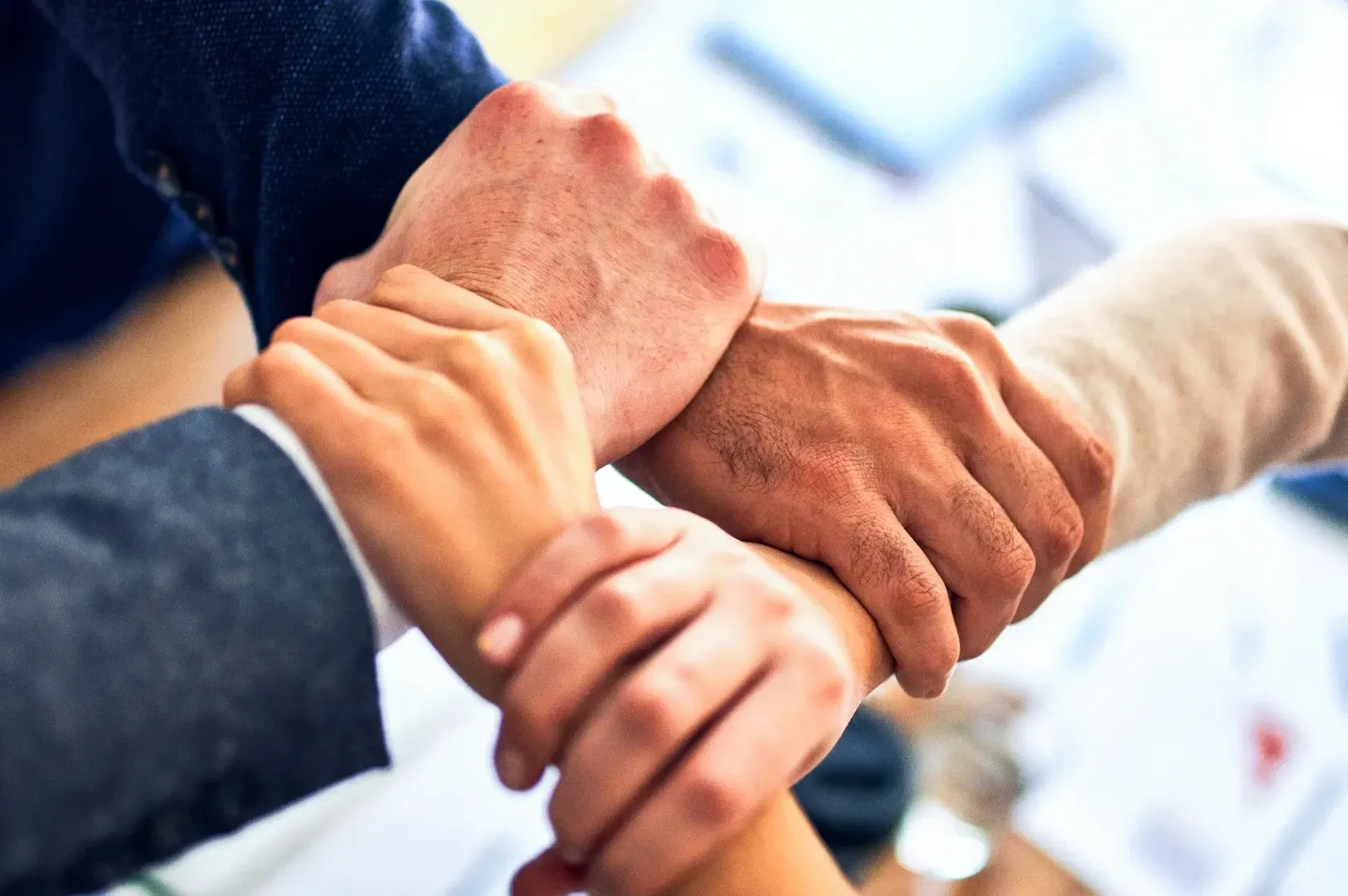Close-up eye-level shot of multiple hands stacked together over a table surface, illustrating teamwork and collaboration in a professional setting.