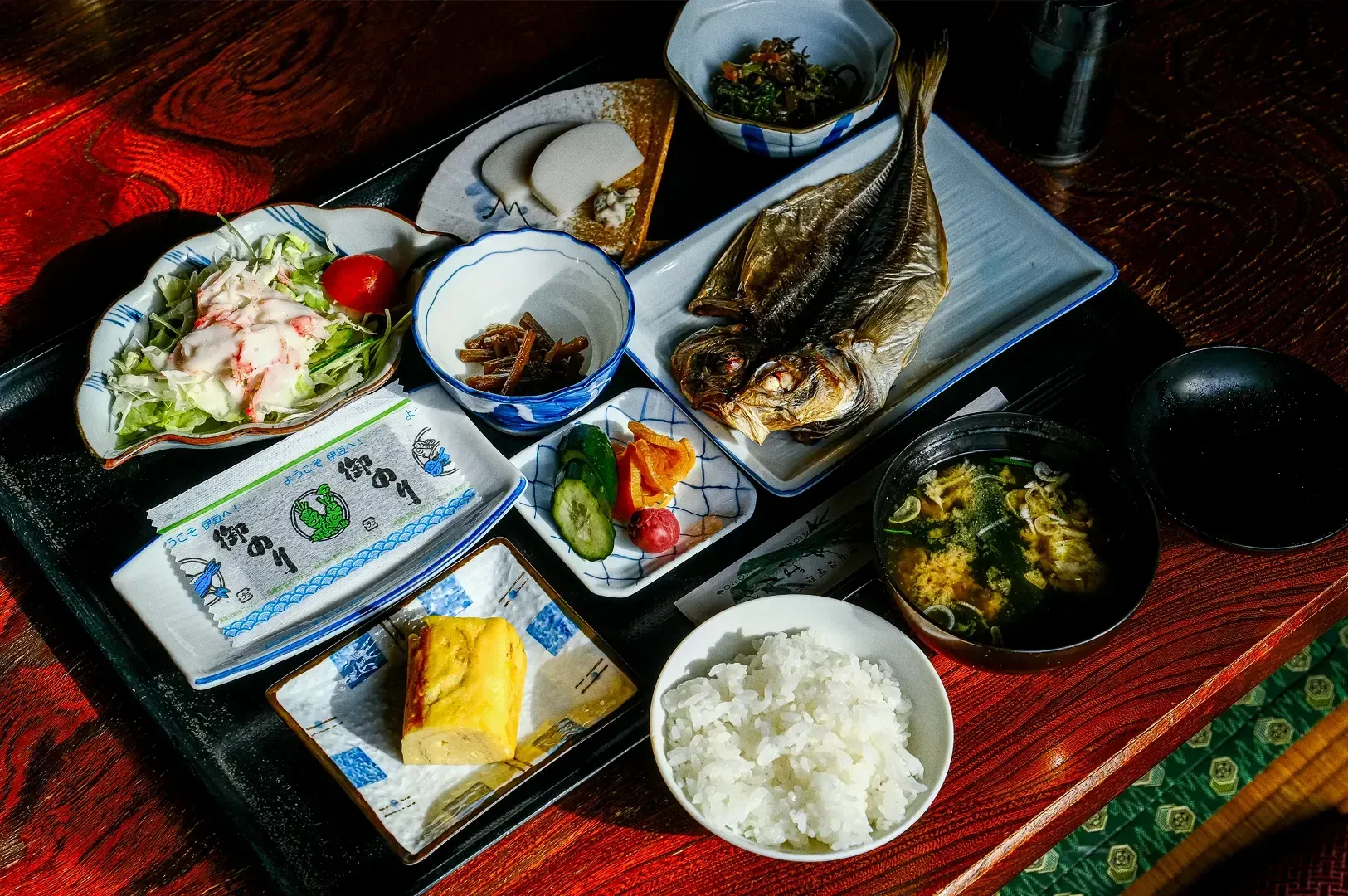 High-angle shot of a traditional Japanese breakfast with grilled fish, rice, miso soup, and small dishes, illustrating mindful travel, cultural respect, and observing local daily rituals in a ryokan setting.