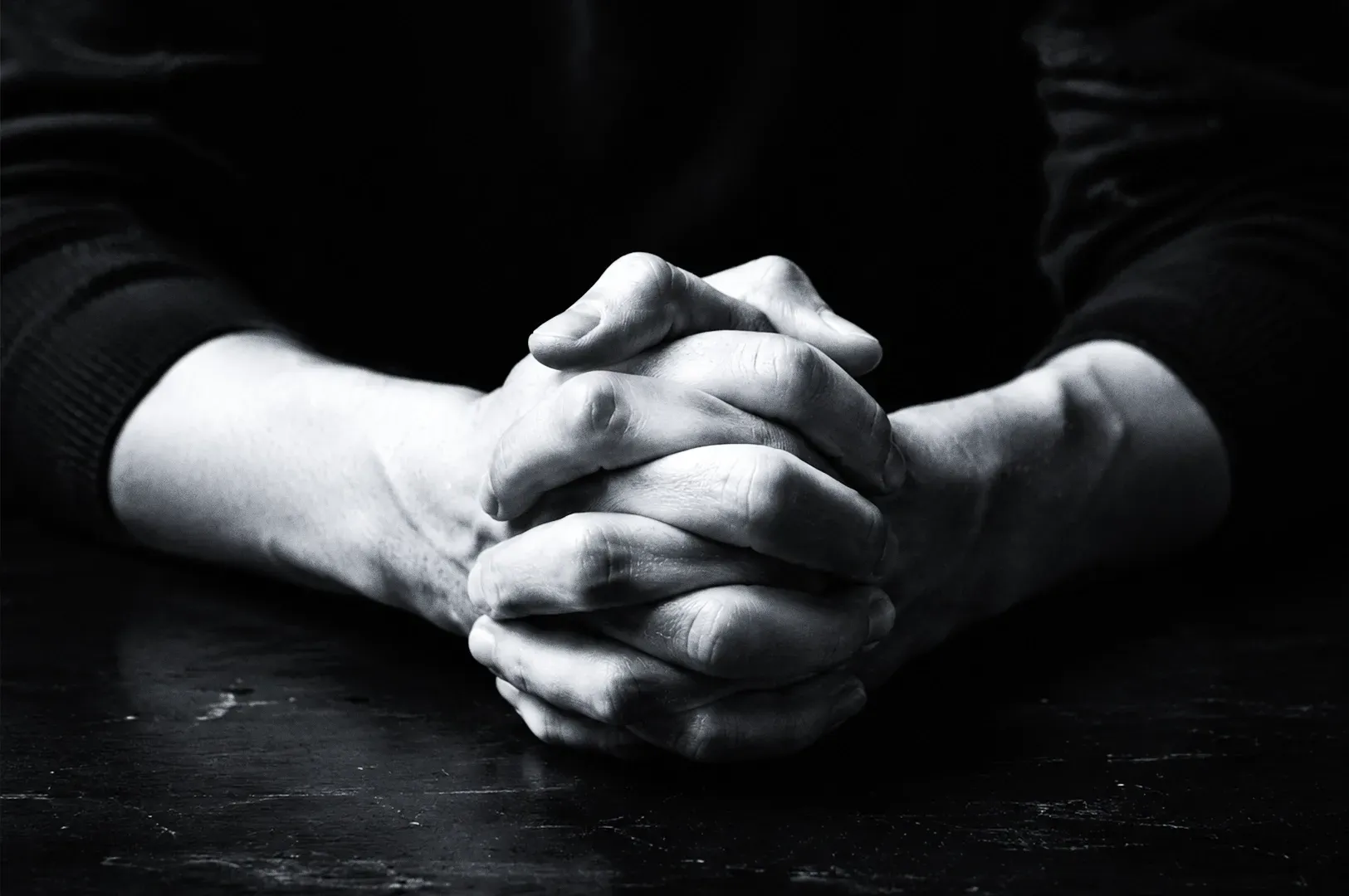 Close-up eye-level shot of clasped hands on a table symbolizing reflective leadership, decision-making, and the founder’s internal struggle between control and trust