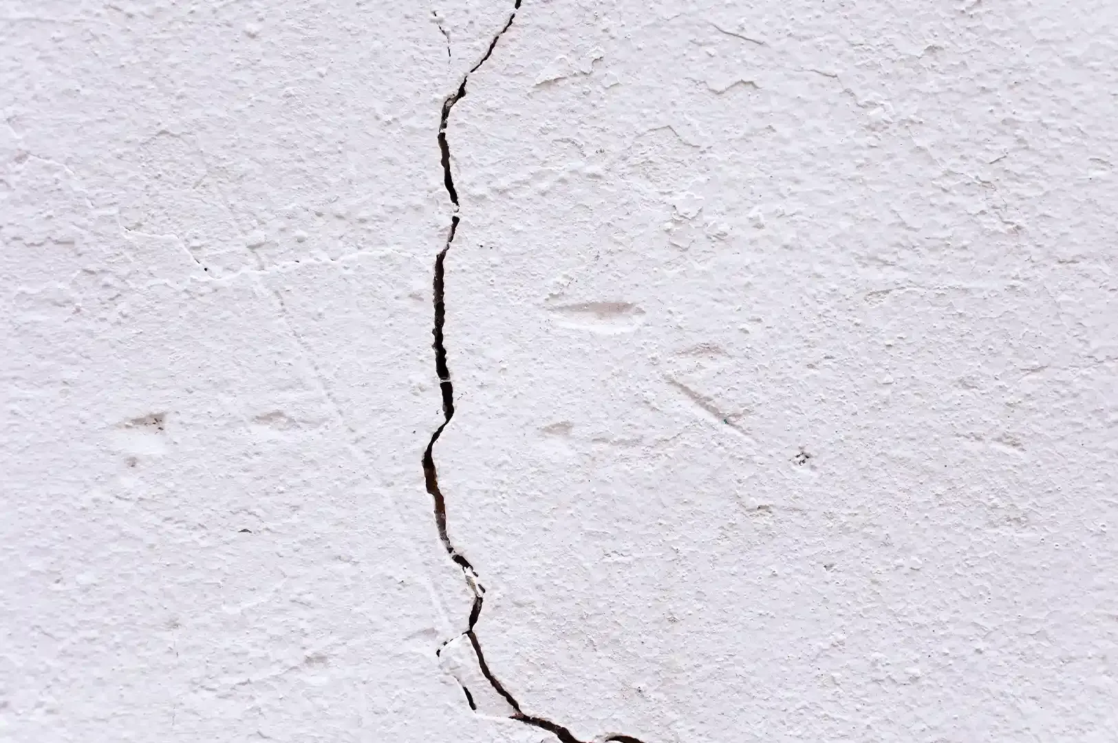 A prominent crack running down a textured white wall, visually metaphorizing how a hard-earned reputation can easily be fractured or diluted.