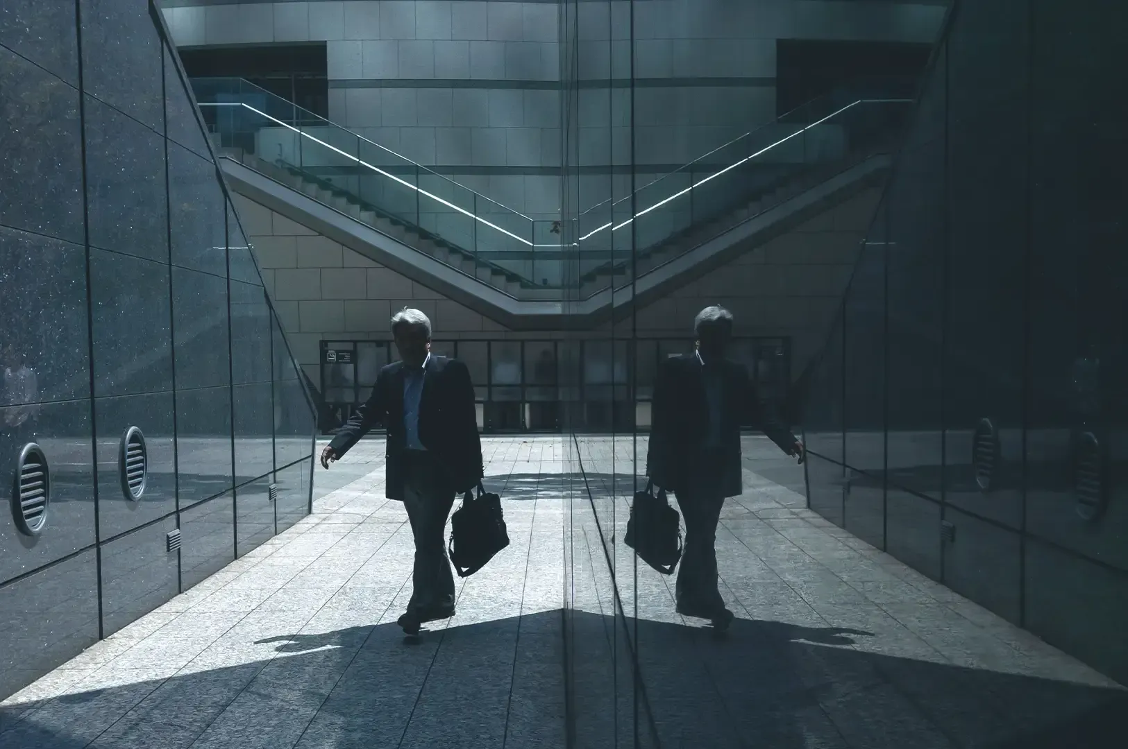 A business professional walking past a mirrored glass building with their reflection clearly visible, representing how a mentor acts as a mirror for personal growth.