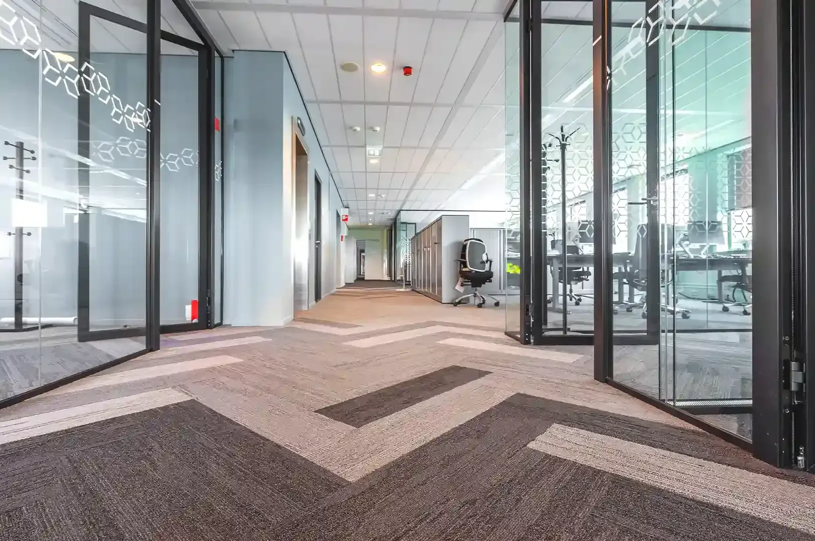 A modern office hallway with glass partition walls and geometric patterned carpeting, reflecting the internal journey from comparison to personal clarity.