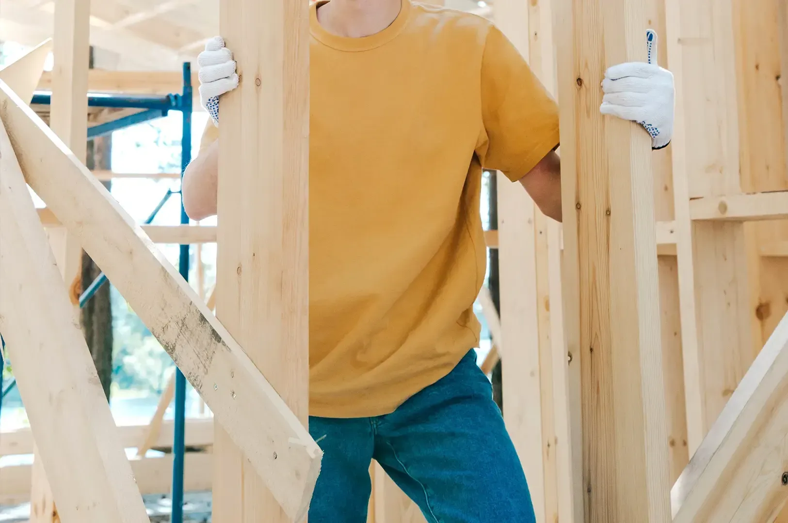 A worker wearing white gloves holding vertical timber beams during framing construction, portraying the physical exertion and integrity required to keep standards high when giving in would be easier.