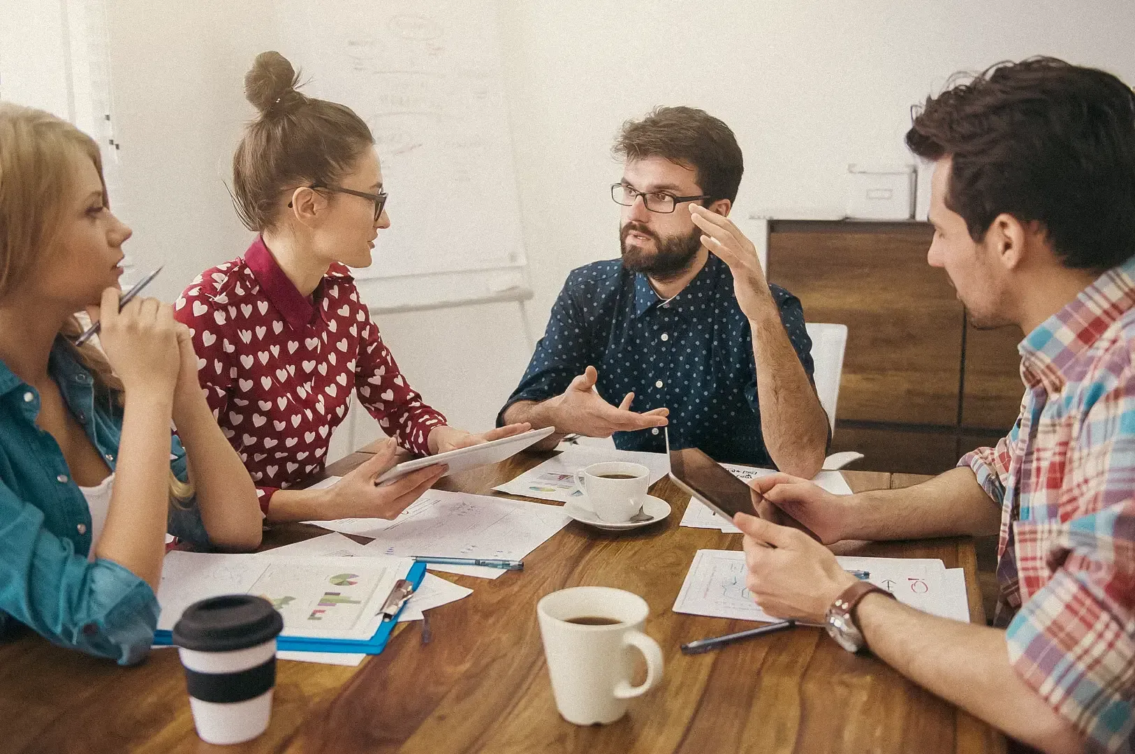 Team meeting around a table with documents, digital devices, and coffee cups as colleagues discuss project ideas.