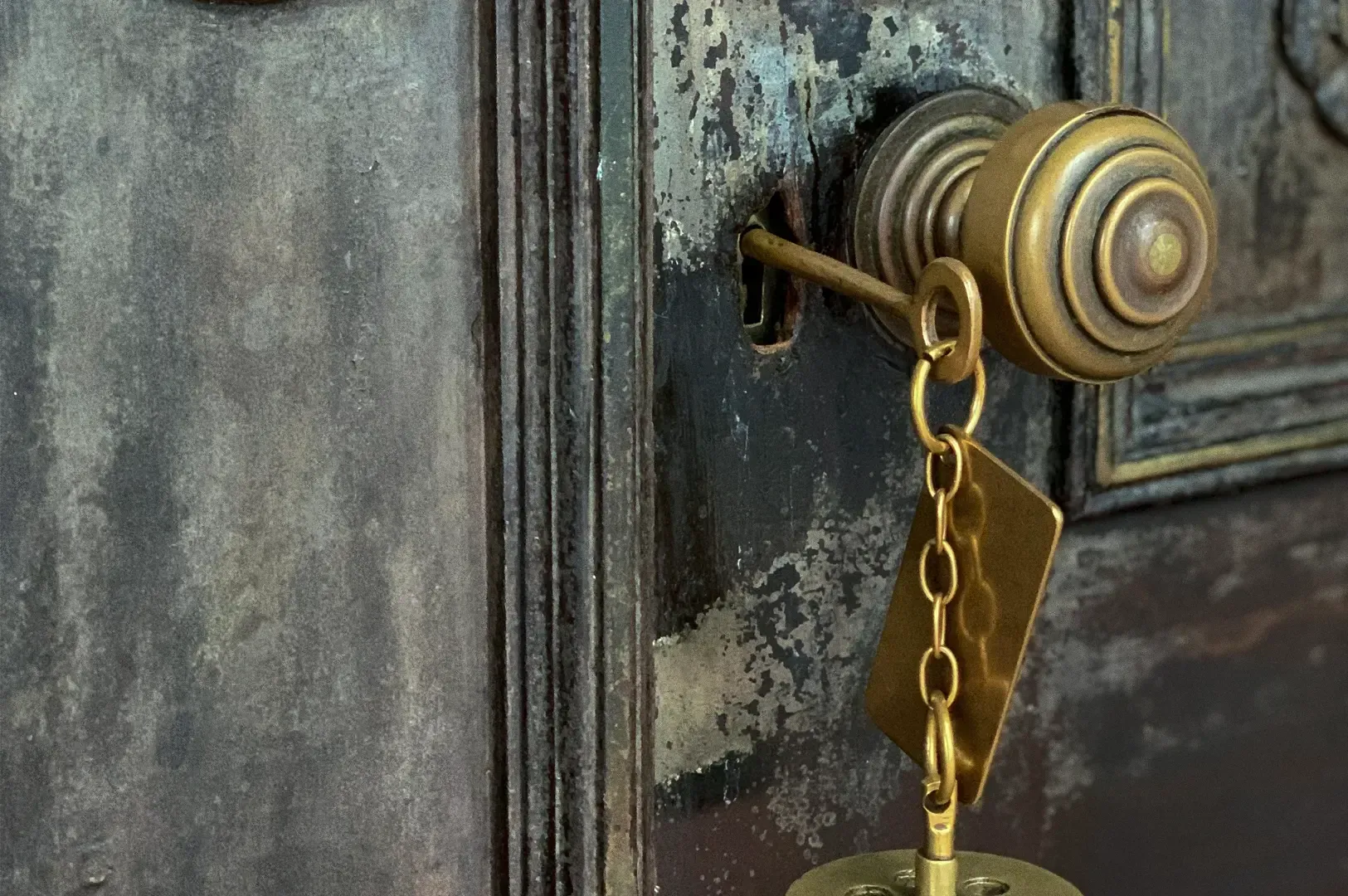 Close-up straight-on shot with slight side perspective of a vintage brass key inserted into an aged metal lock, emphasizing textured patina and antique detail.
