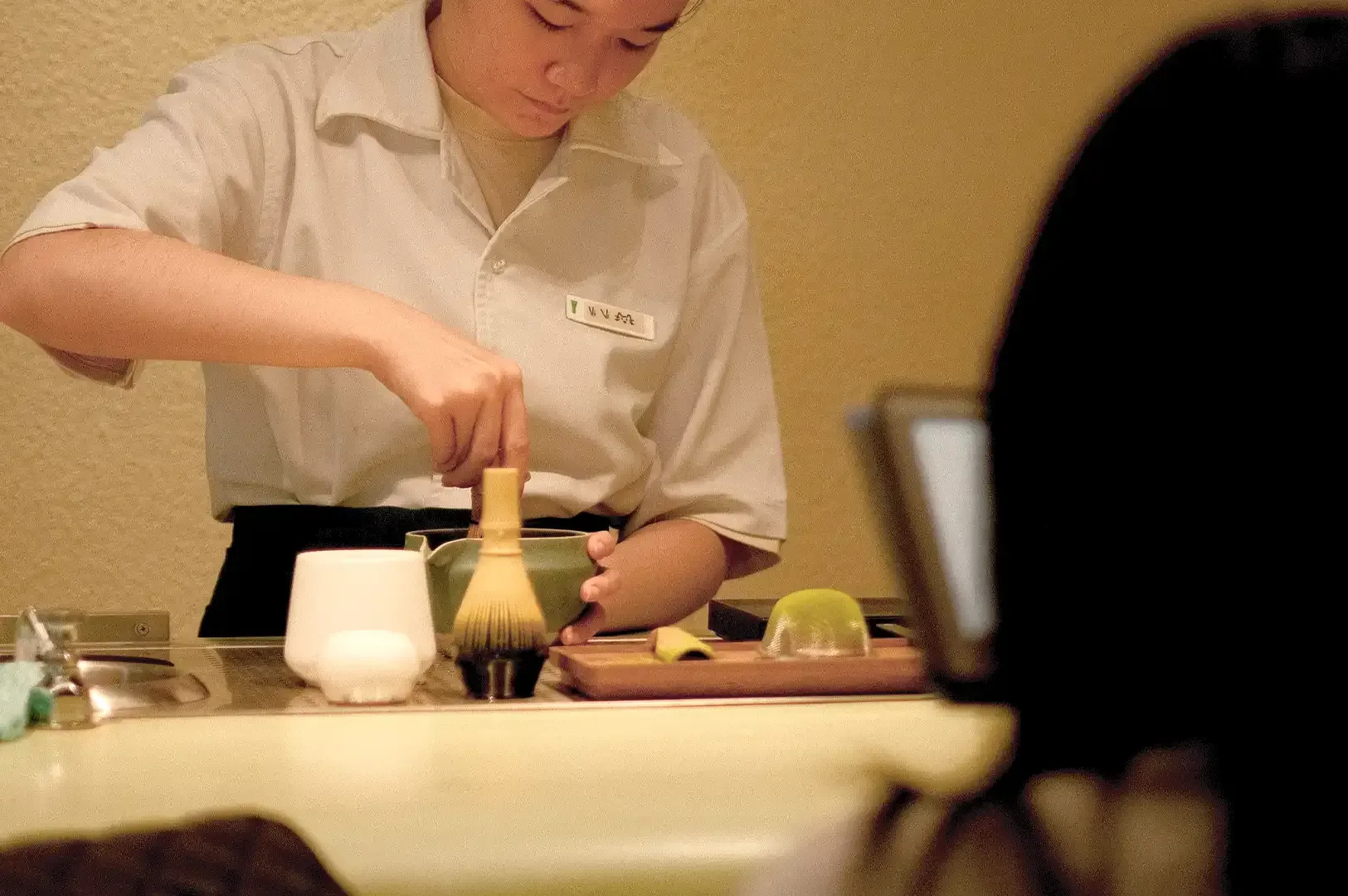 A person focused on preparing matcha with traditional tools, serving as a metaphor for partnership as a quiet, deliberate practice of character and mastery.