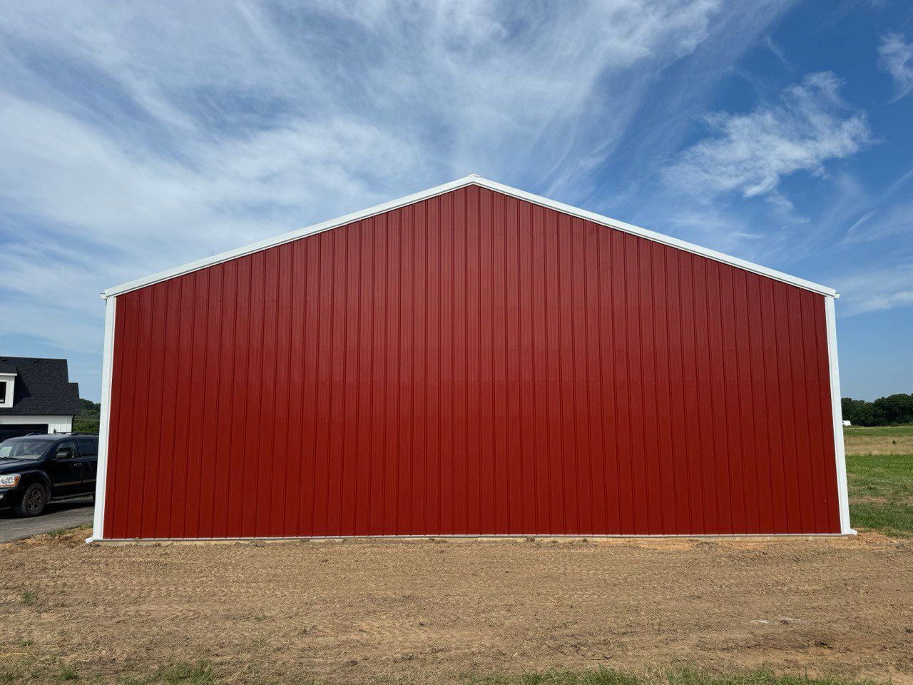A red barn with a white trim is sitting in the middle of a dirt field.