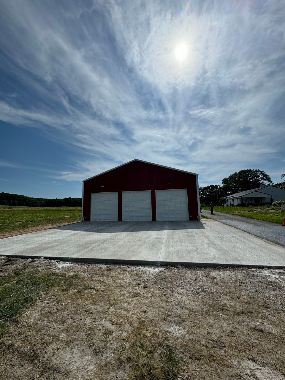 A red barn with three garage doors is sitting on top of a concrete driveway.