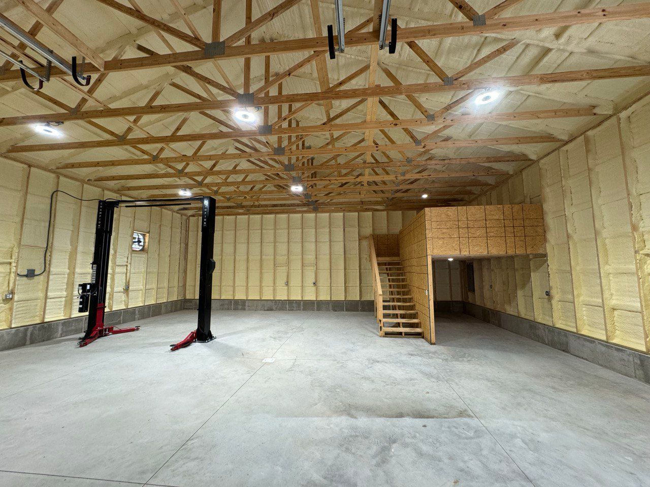 A large empty garage with a lift and stairs.