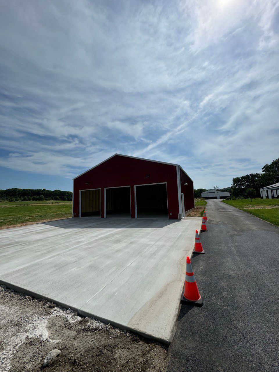 A red barn is sitting on the side of a road next to a concrete driveway.