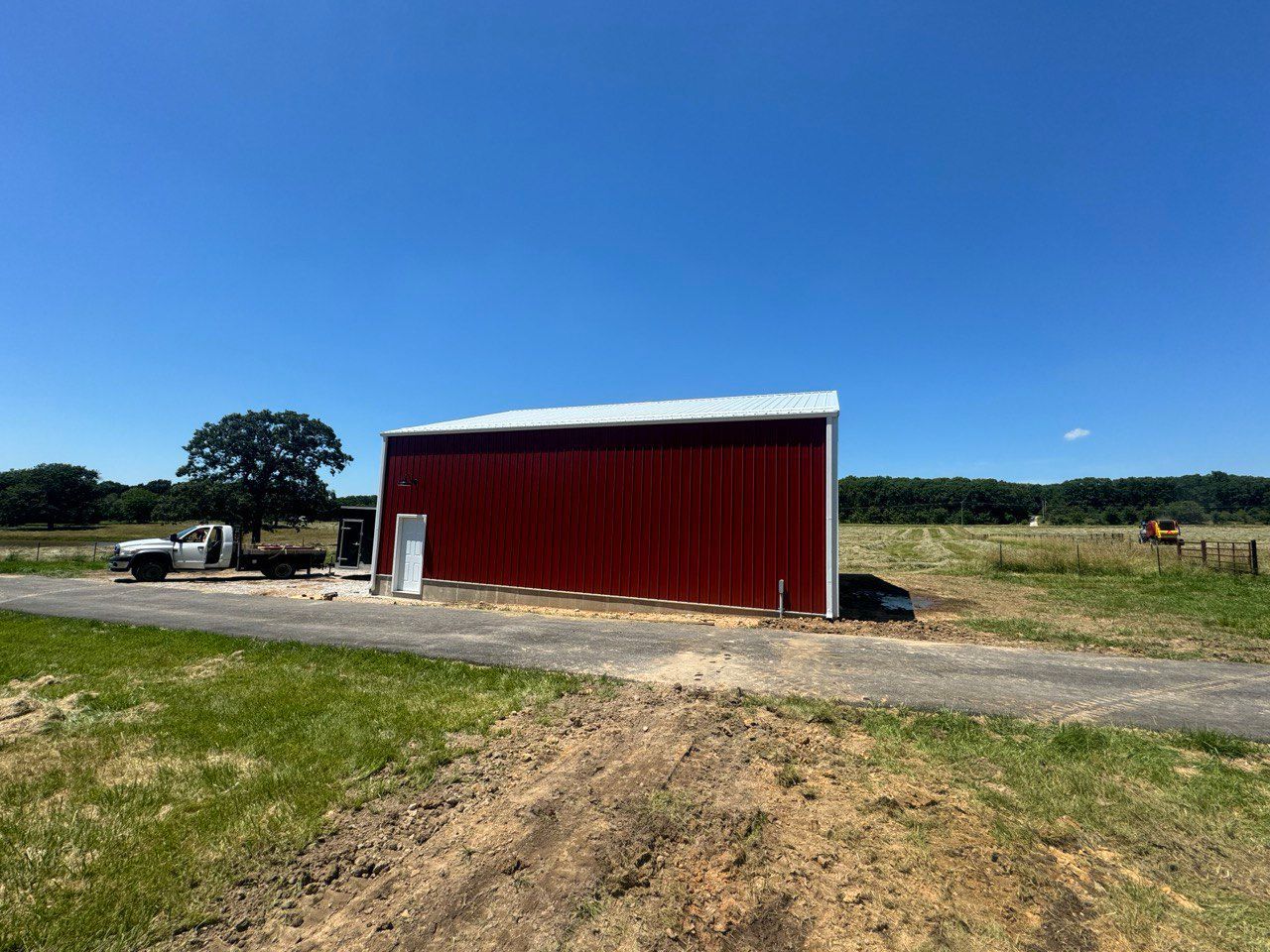 A red barn is sitting on the side of a dirt road in a field.