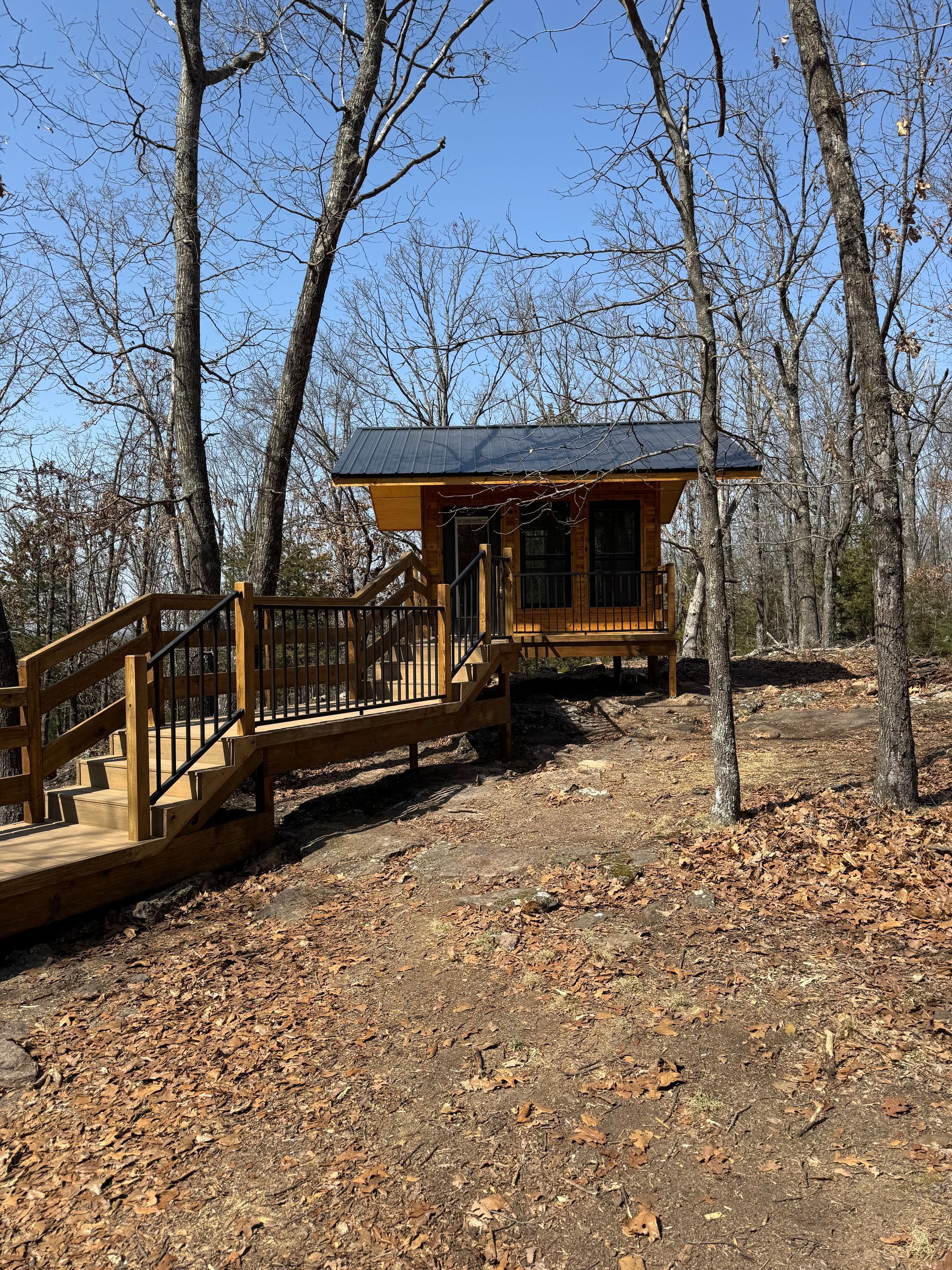 A small cabin in the middle of a forest with a wooden deck.