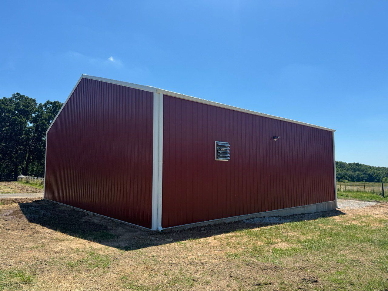 A red barn with a white trim is sitting in the middle of a grassy field.