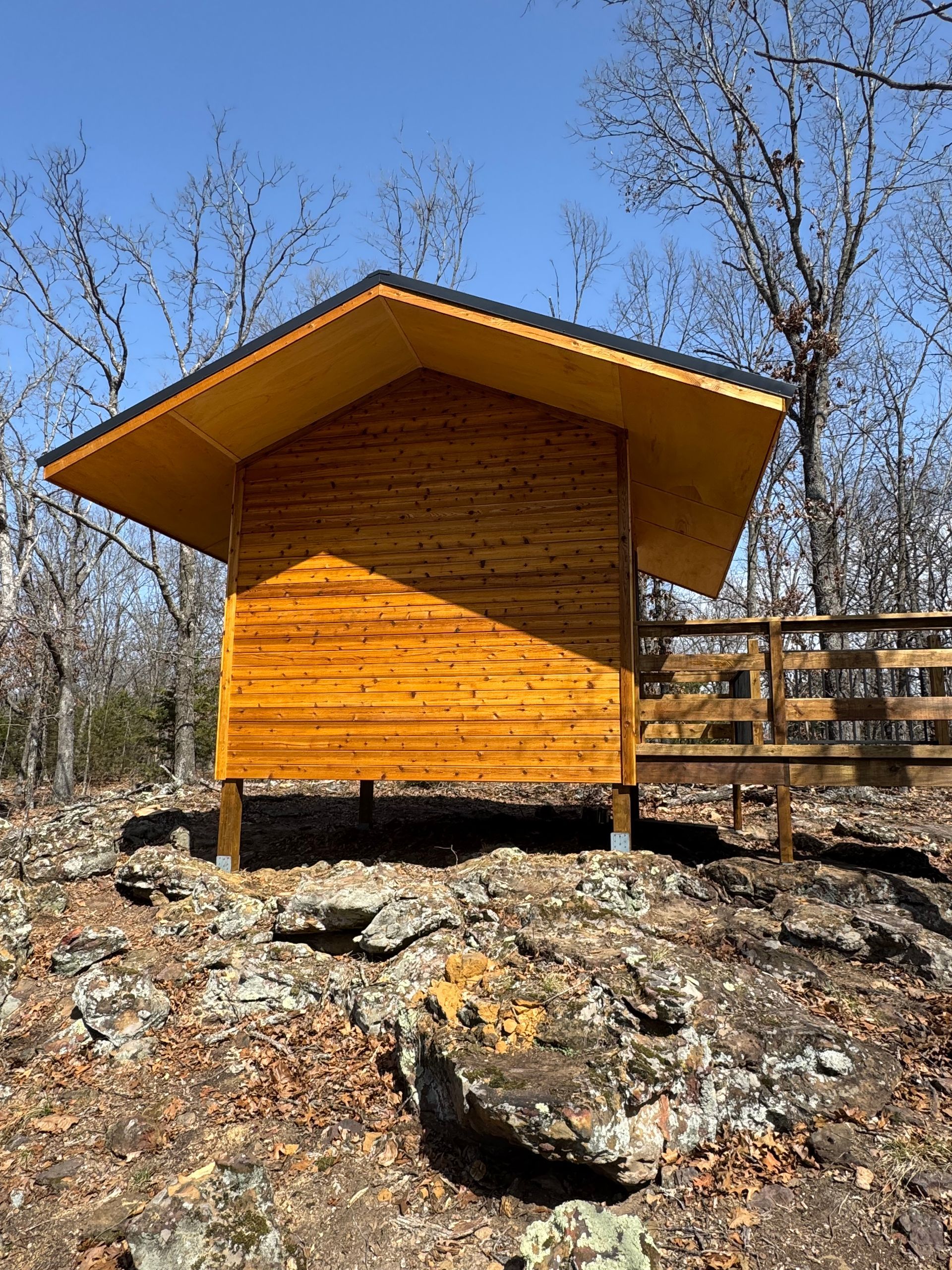 A small wooden hut is sitting on top of a rocky hill in the woods.