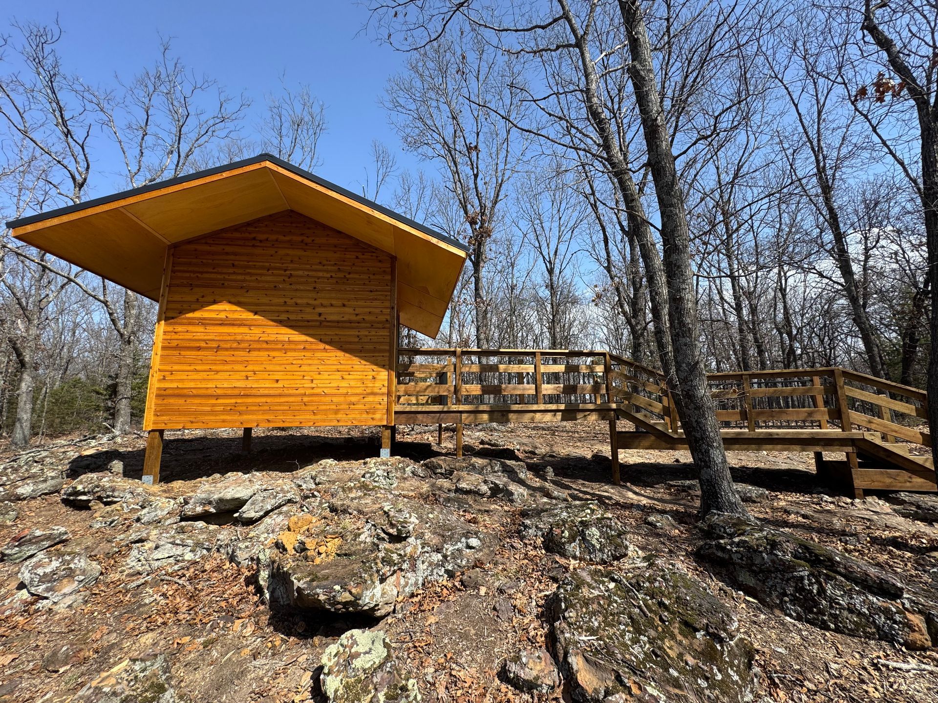 A small wooden cabin with a wooden deck in the middle of a forest.