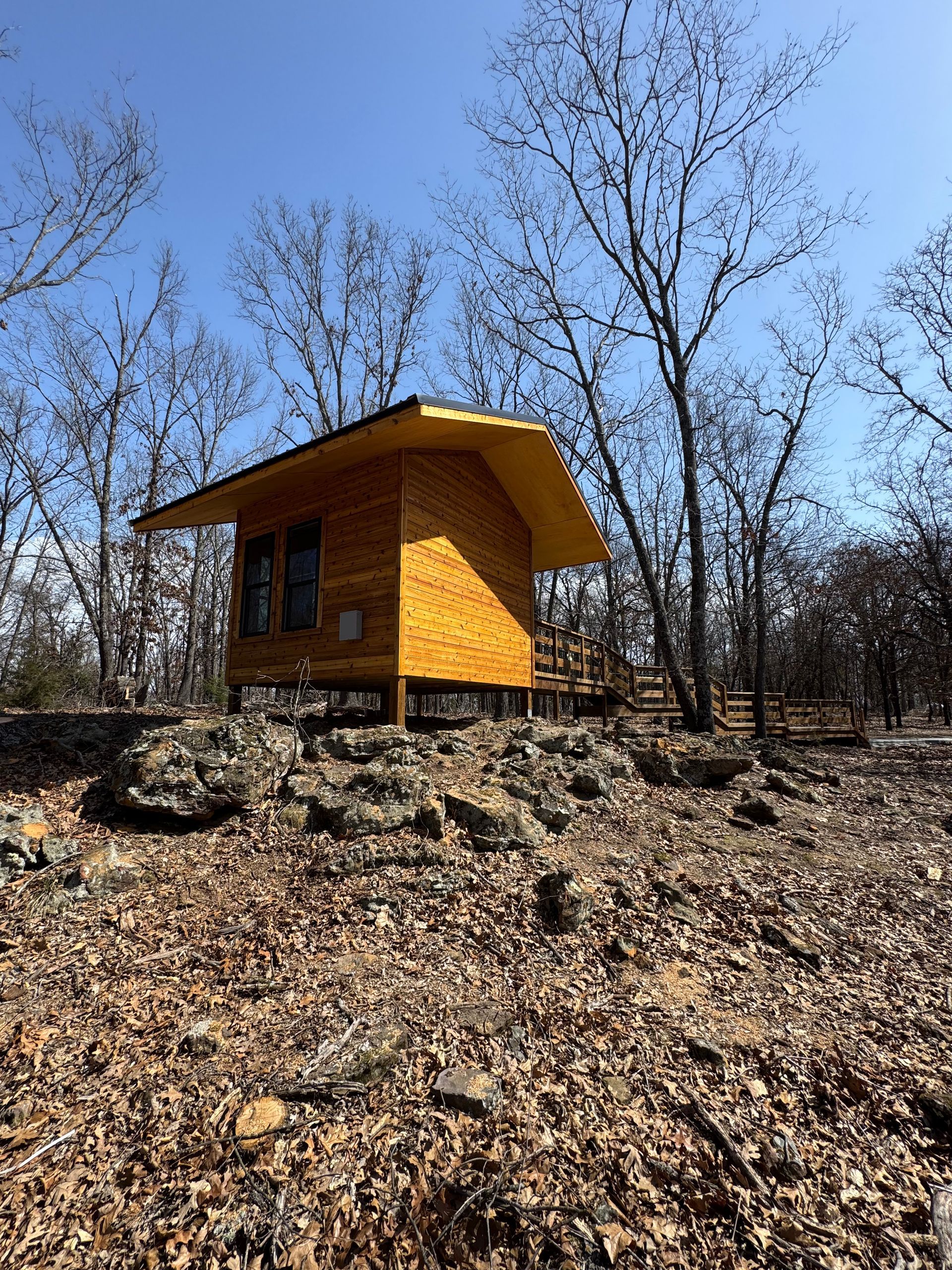 A small wooden cabin is sitting on top of a rocky hill in the middle of a forest.