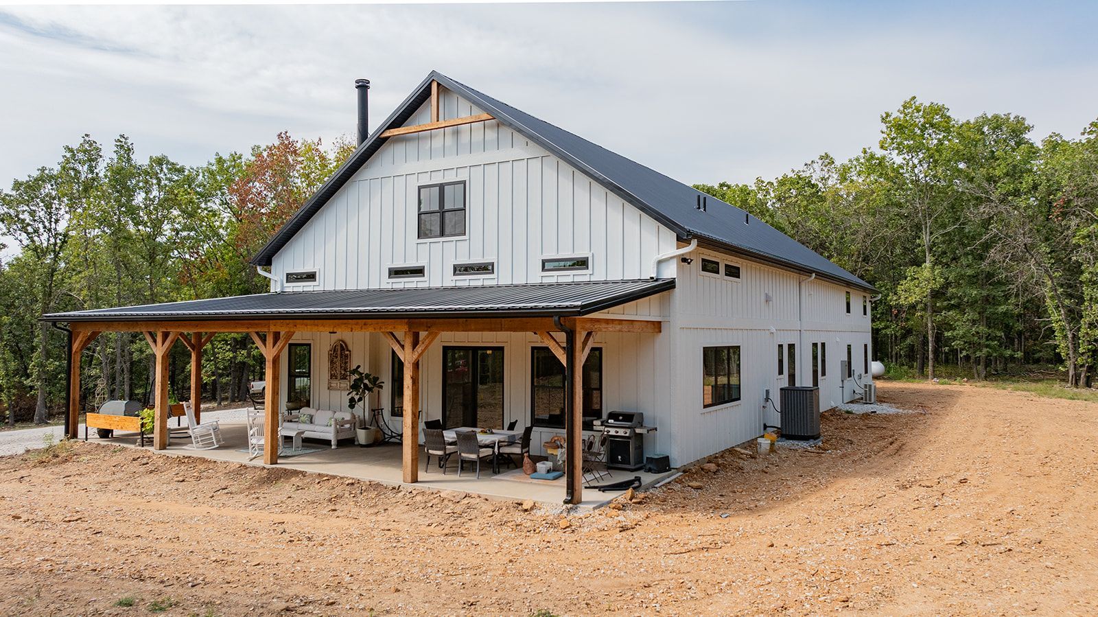 A large white barn with a porch and trees in the background.