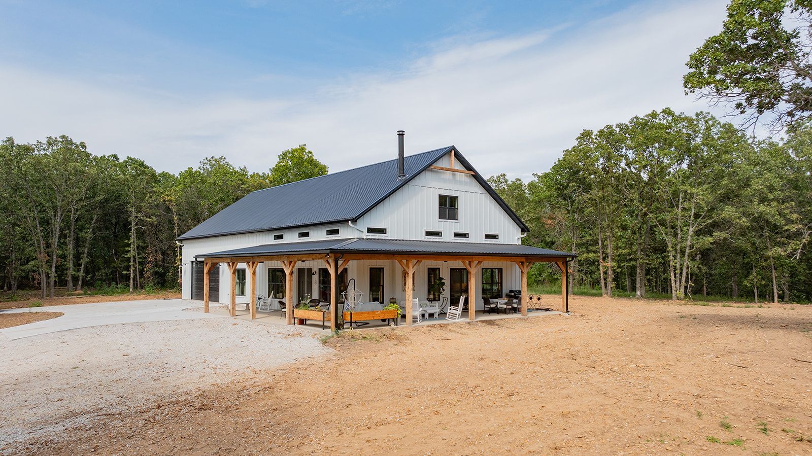 A white house with a black roof is sitting in the middle of a dirt field.