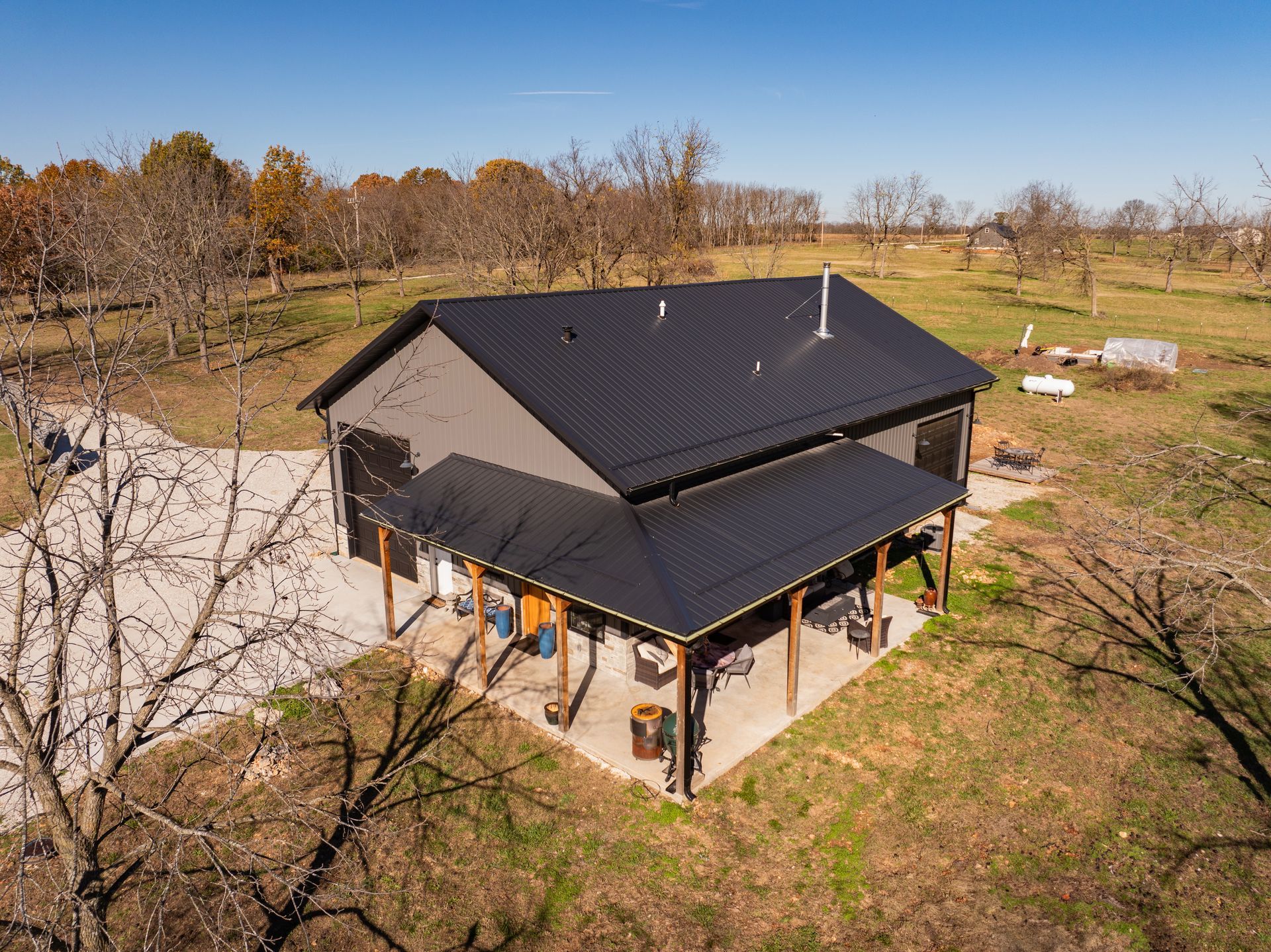 An aerial view of a house with a black roof in the middle of a field.