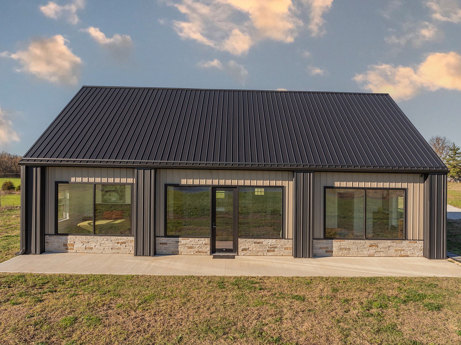A house with a black roof and a lot of windows is sitting in the middle of a field.
