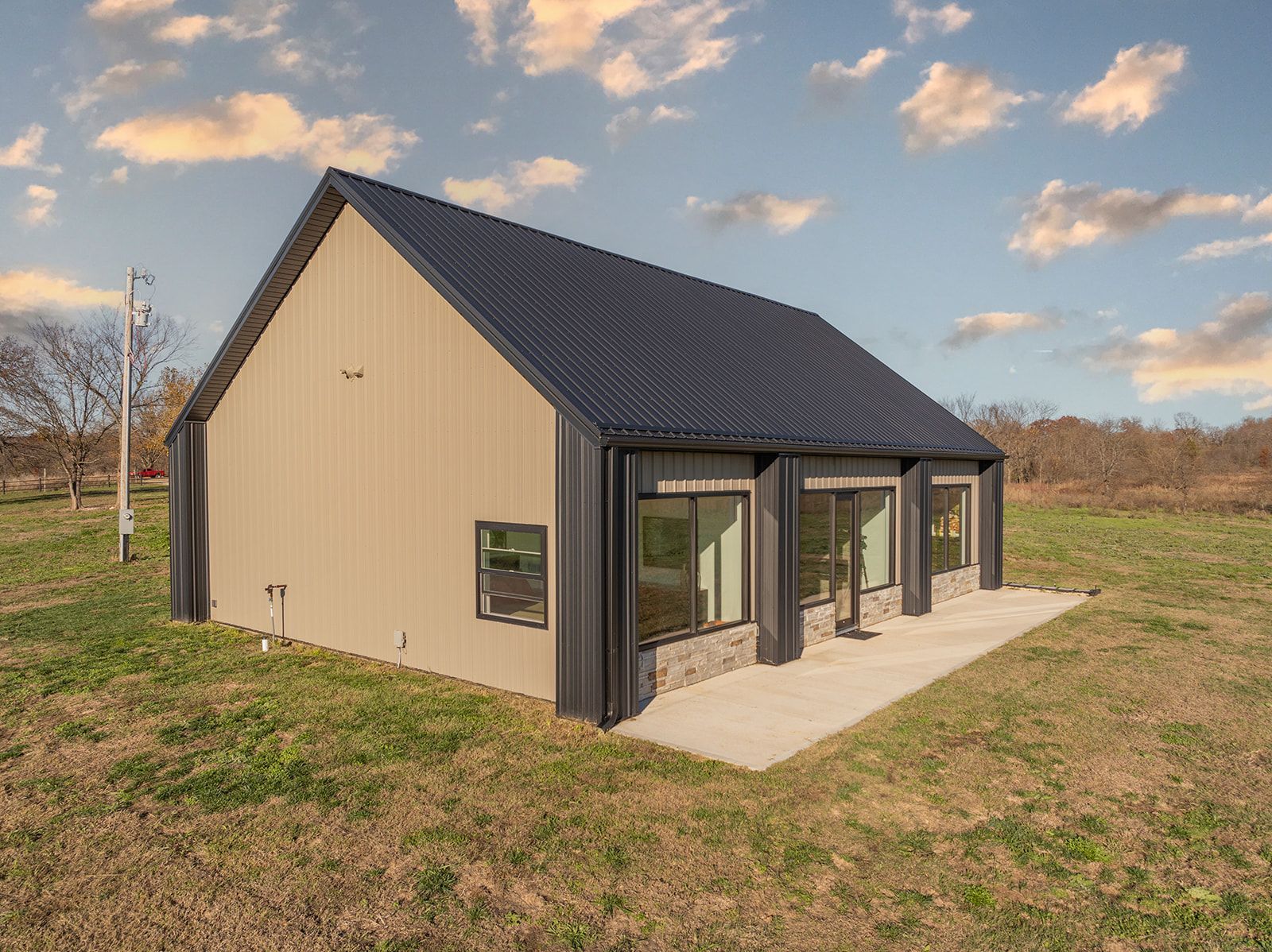 A small house with a black roof is sitting in the middle of a grassy field.