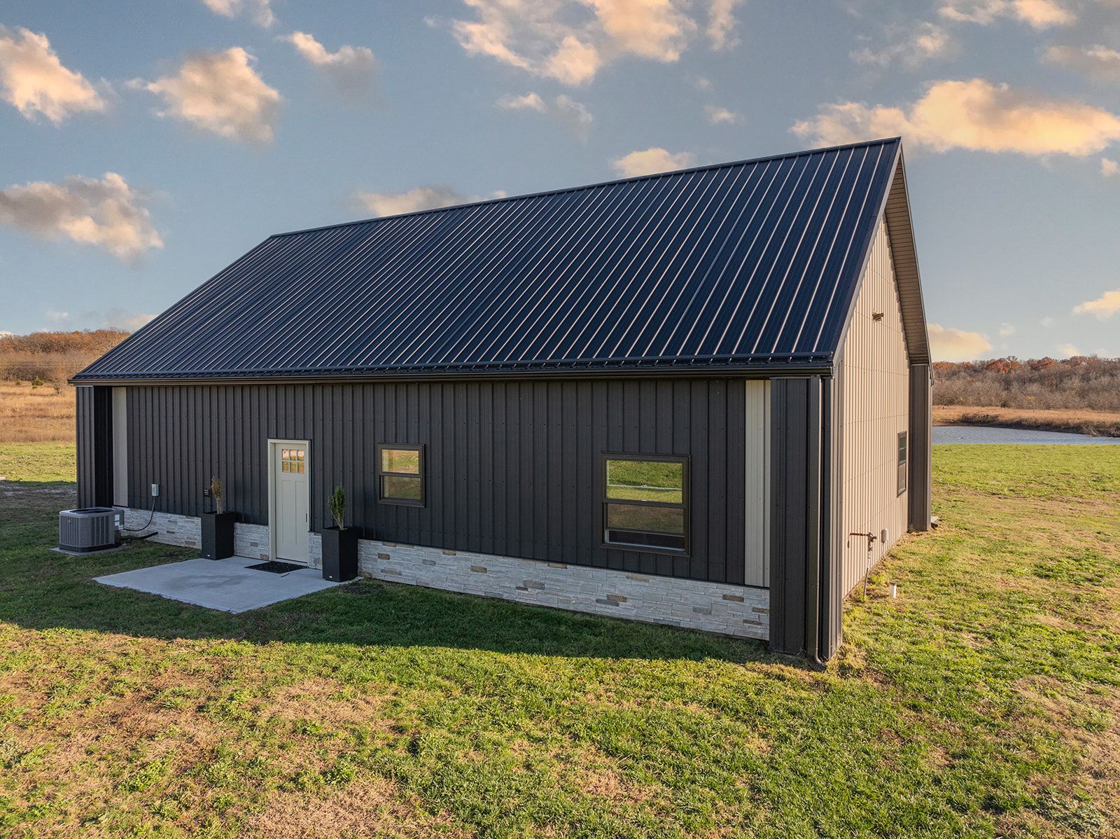 A small black barn is sitting in the middle of a grassy field.